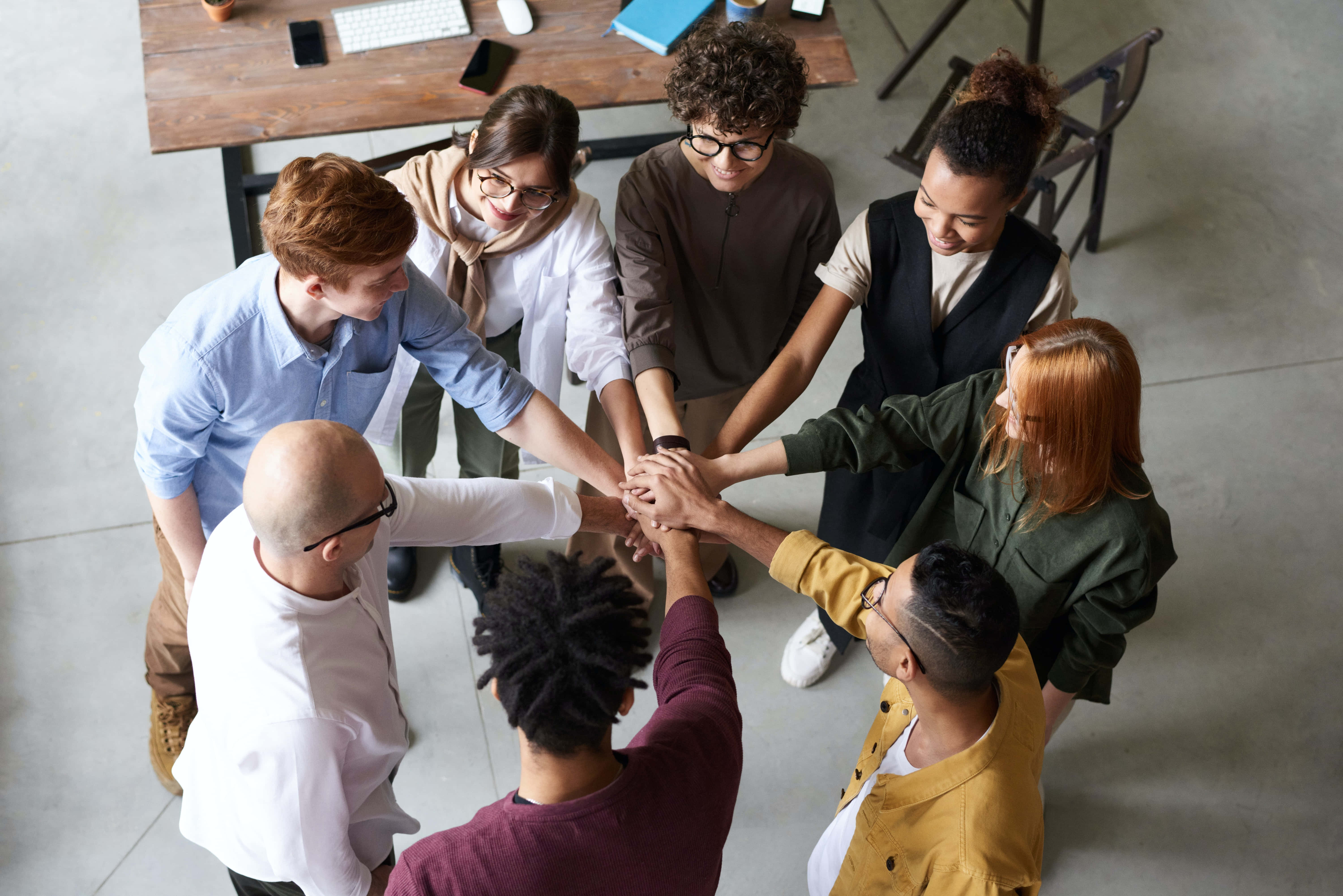 Teamwork 桌布 壁紙 — 多元化的專業團隊在現代辦公室聚集，將手疊成圓圈以展示團結與協作。