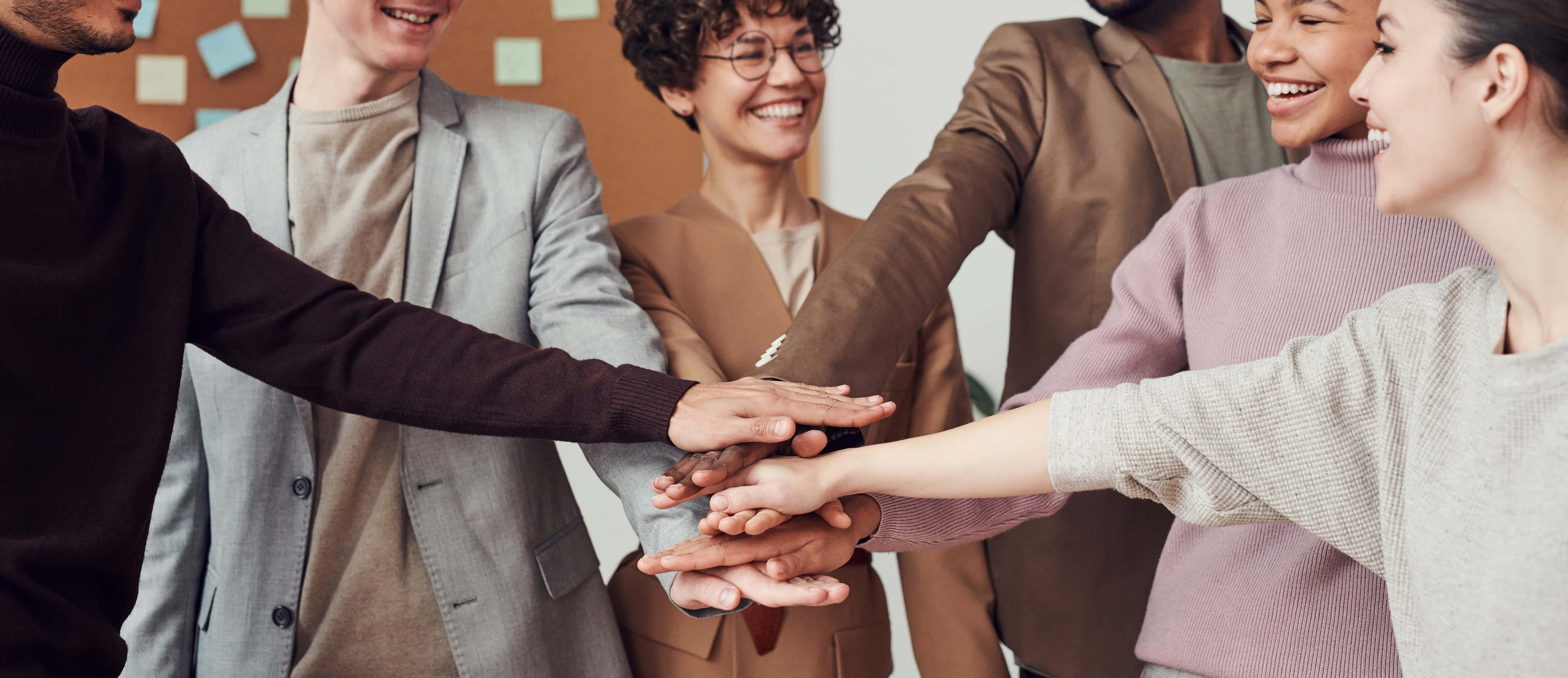 Teamwork 桌布 壁紙 — 多元化的微笑團隊成員以統一的合作與成功手勢疊手。