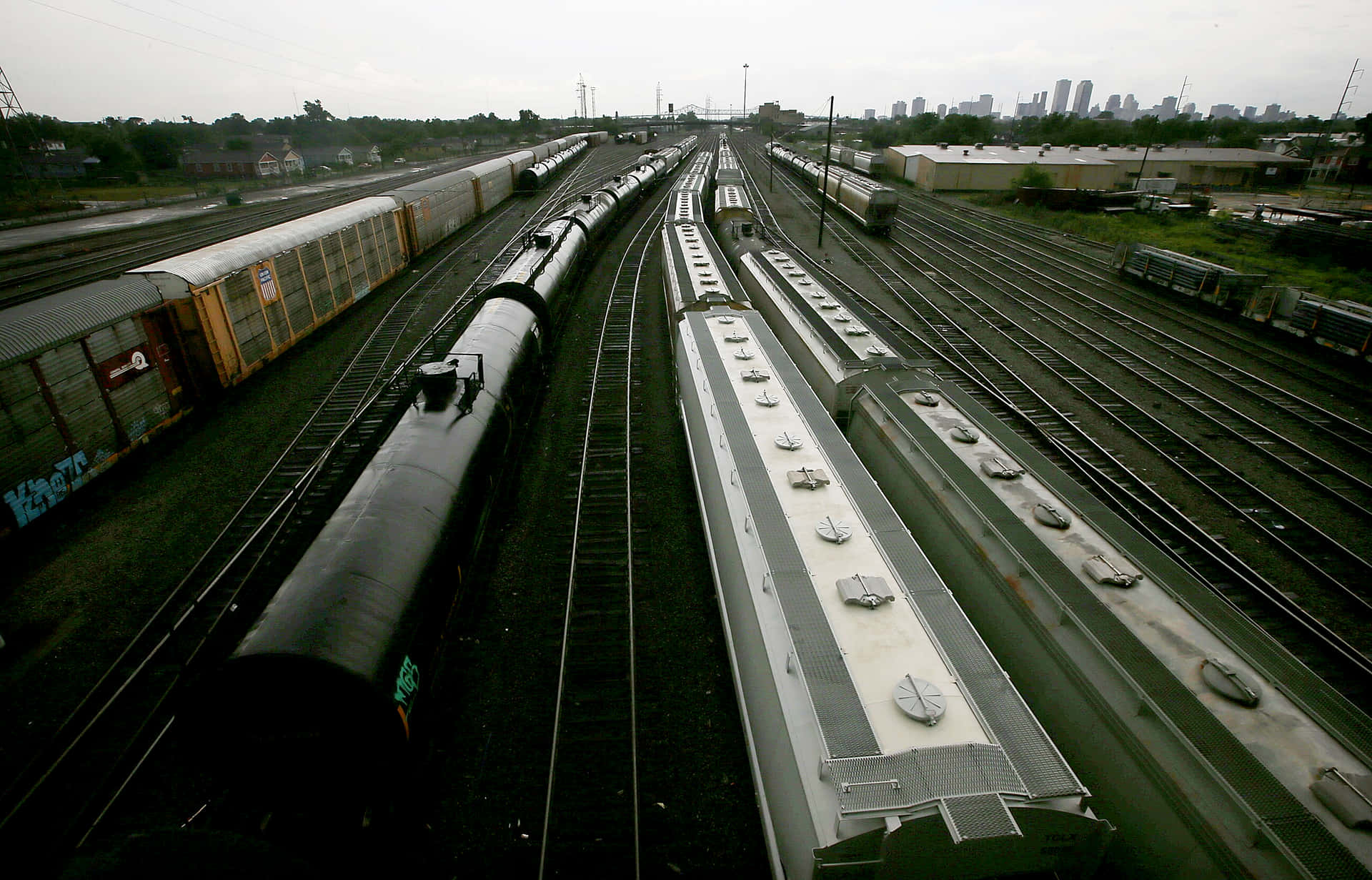 攝影 桌布 壁紙 — 多列貨運列車在工業鐵路調車場的平行軌道上，遠處城市天際線在陰天下的空拍視圖。