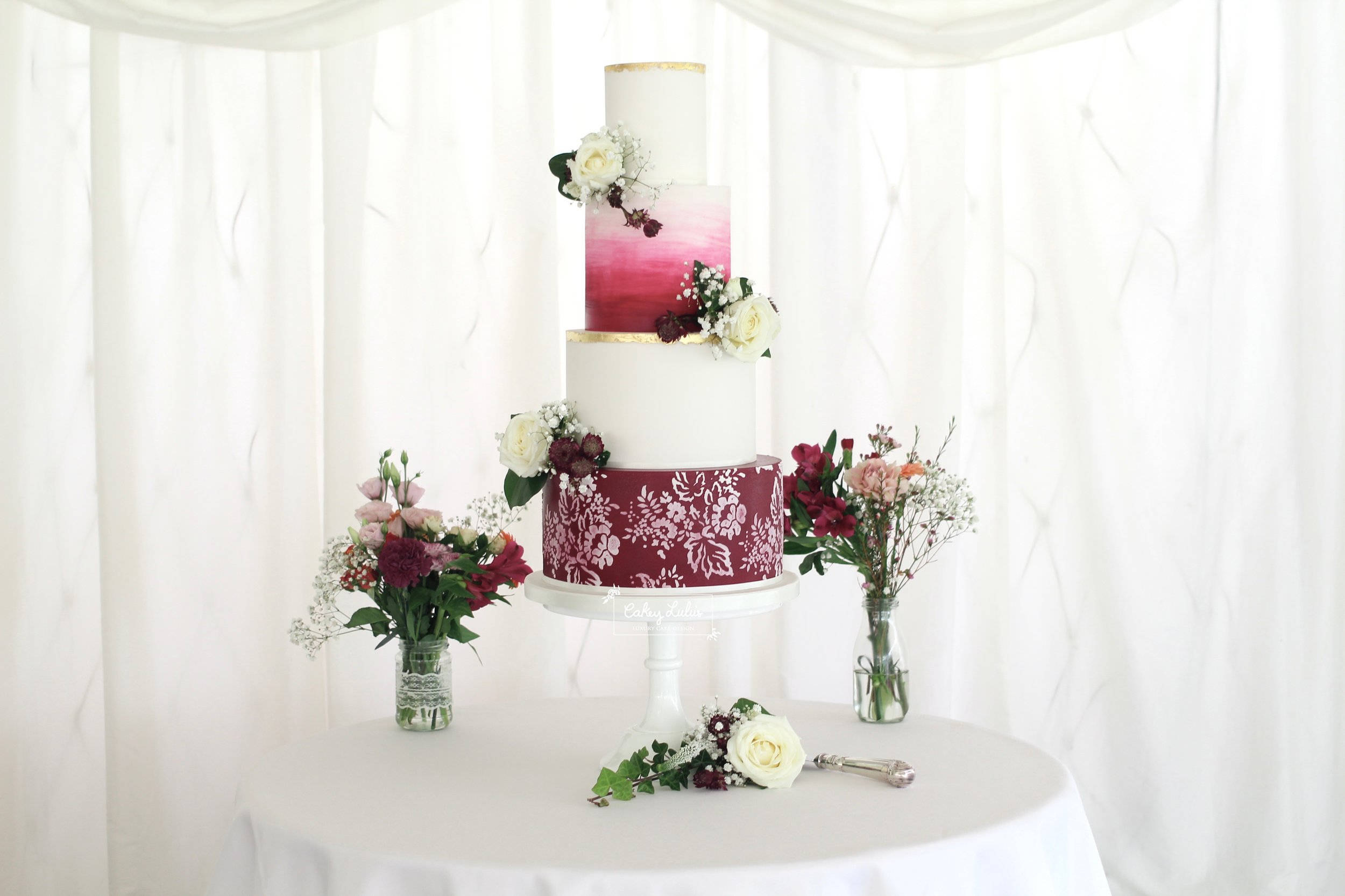 Wedding 桌布 壁紙 — 多層結婚蛋糕，帶有漸層粉紅和酒紅色層次，飾以白色花朵，優雅地立於白色桌布上。
