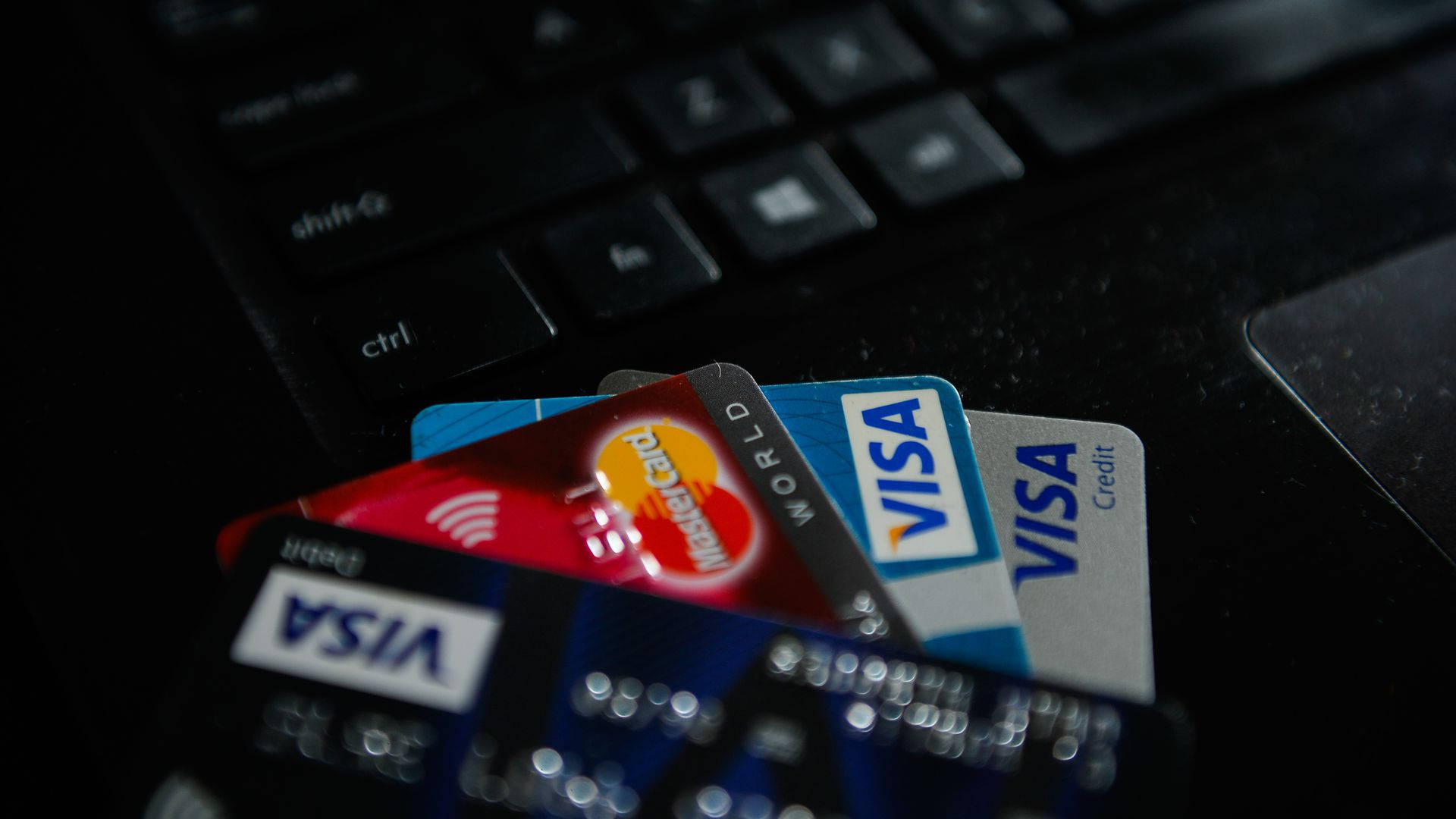 Credit Card 桌布 壁紙 — 多張信用卡在深色筆記型電腦鍵盤上呈扇形展開的特寫，景深較淺。