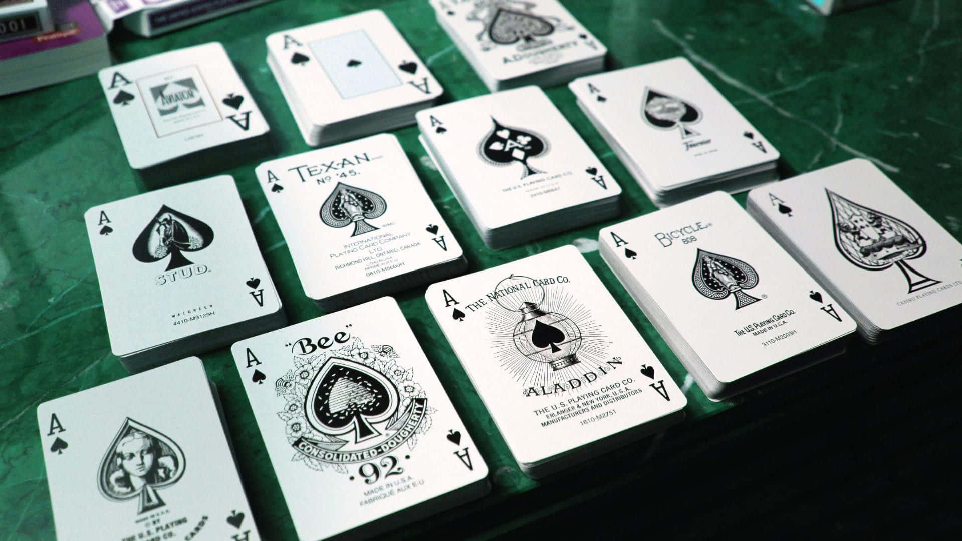 Card Games 桌布 壁紙 — 多張具有獨特藝術設計的黑桃A撲克牌散落在綠色毛氈表面上。