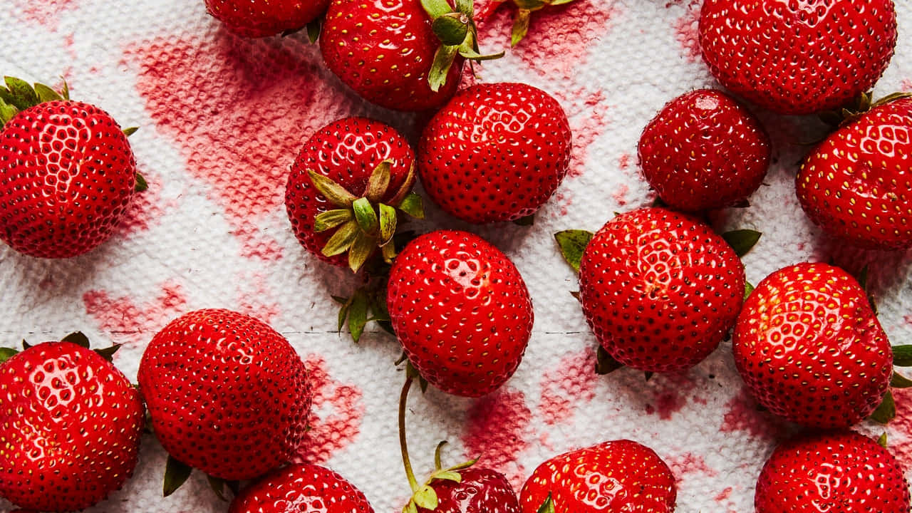 Strawberries 桌布 壁紙 — 多汁成熟的草莓，帶有綠色蒂頭，散落在沾有紅色果汁的白色紋理毛巾上。