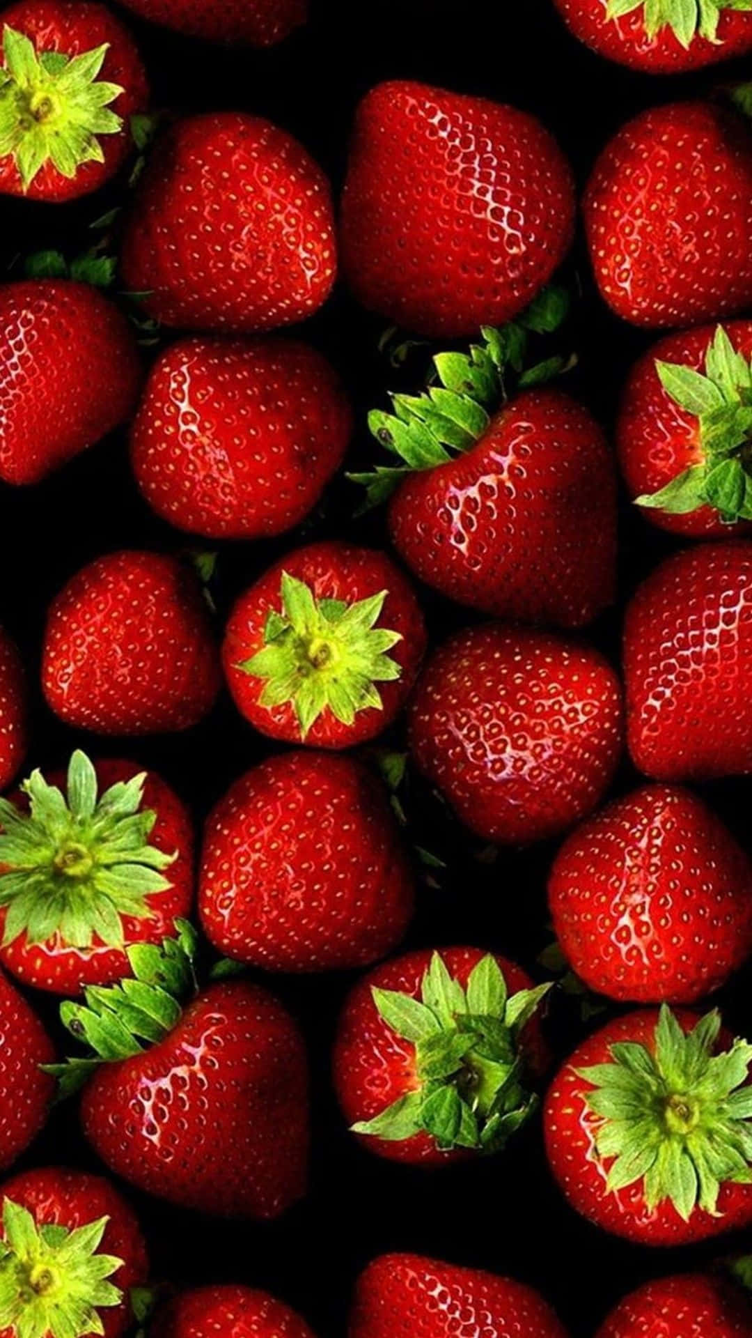 Red Strawberry 桌布 壁紙 — 多汁成熟的草莓，帶有綠色頂部，緊密排列在黑色背景上。