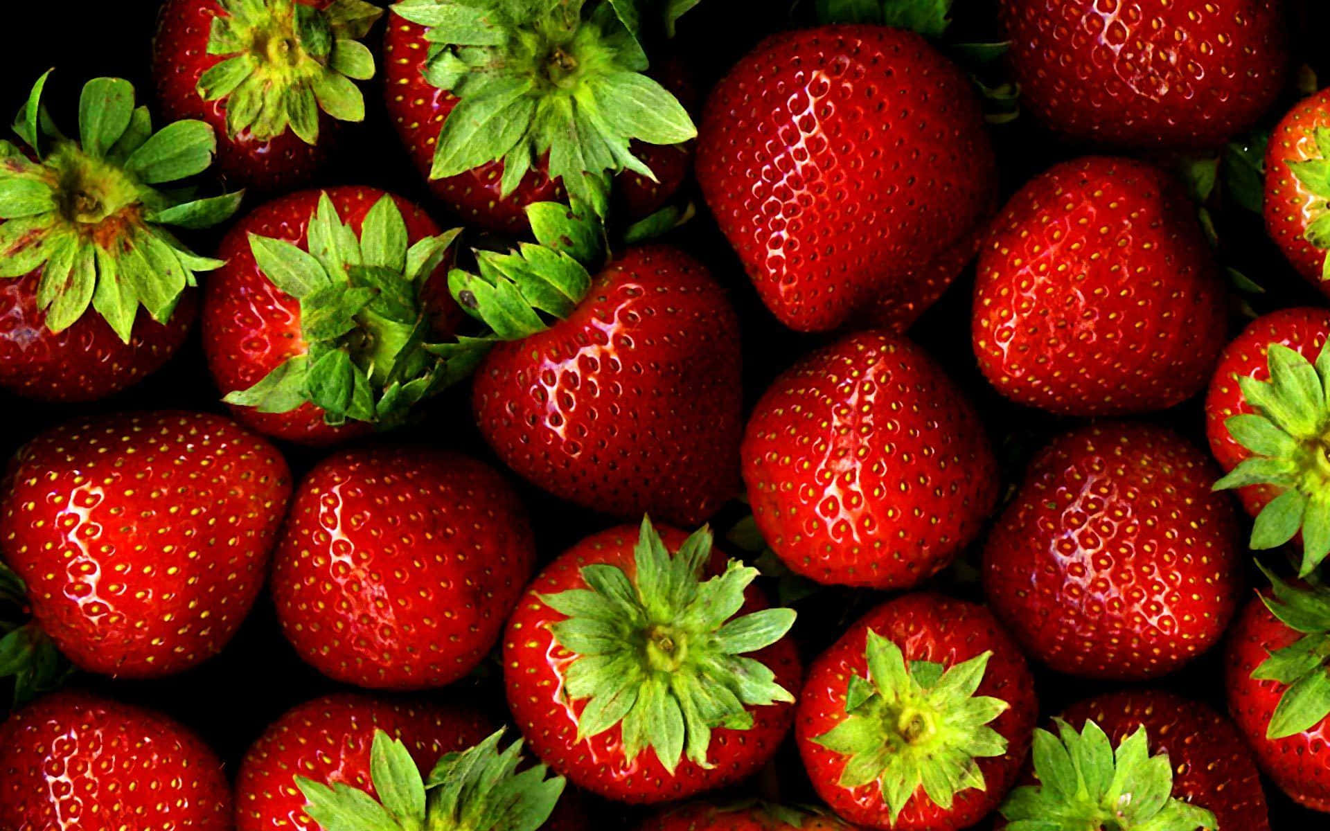Red Strawberry 桌布 壁紙 — 多汁成熟的草莓，帶有鮮綠色頂部，緊密堆疊在深色背景上。