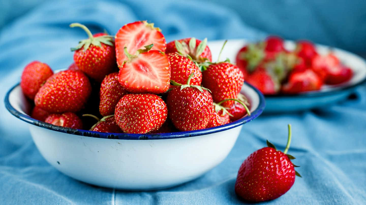 Strawberries 桌布 壁紙 — 多汁成熟的草莓堆放在白色琺瑯碗中，放在有紋理的藍色布上，旁邊放著一顆草莓。