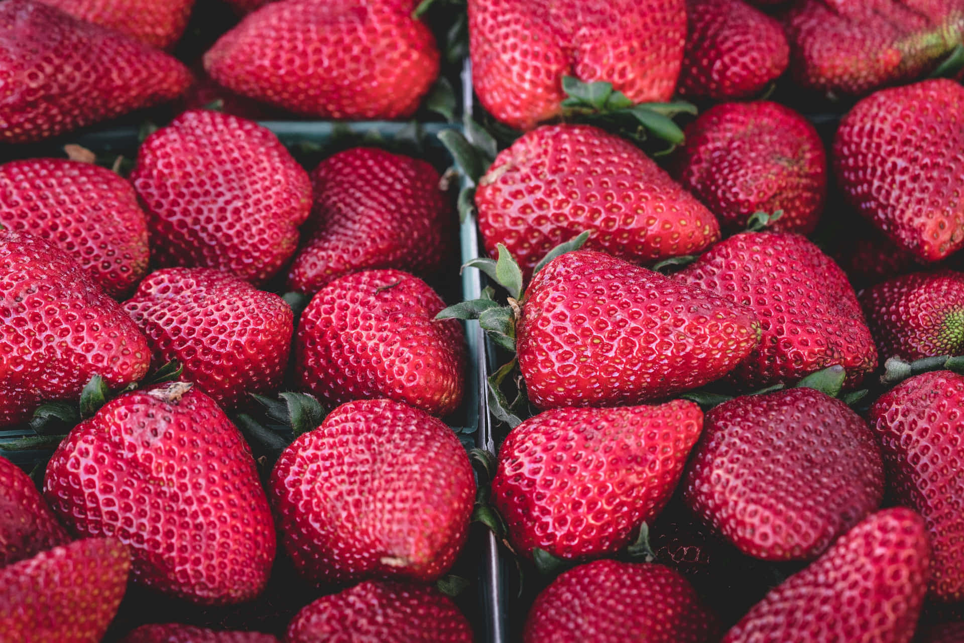Strawberry 桌布 壁紙 — 多汁成熟的草莓帶有綠色莖部，堆疊在黑色托盤中，在柔和光線下閃閃發光。