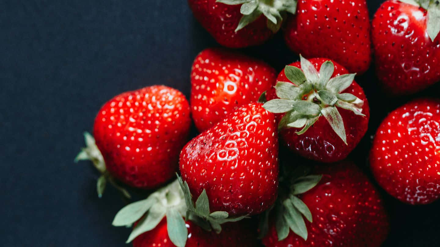 Strawberries 桌布 壁紙 — 多汁成熟的草莓帶有綠色蒂頭，在深色紋理背景上閃閃發光。