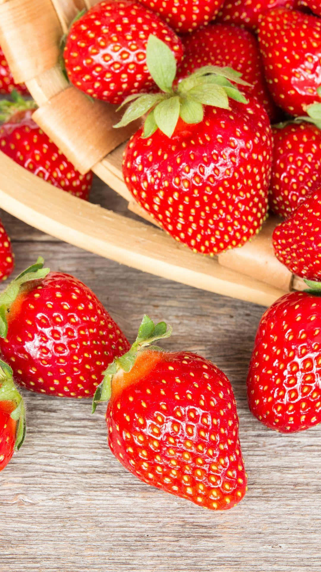 Red Strawberry 桌布 壁紙 — 多汁成熟的草莓帶有綠色蒂頭，從編織籃子溢出到風化的木質表面上。