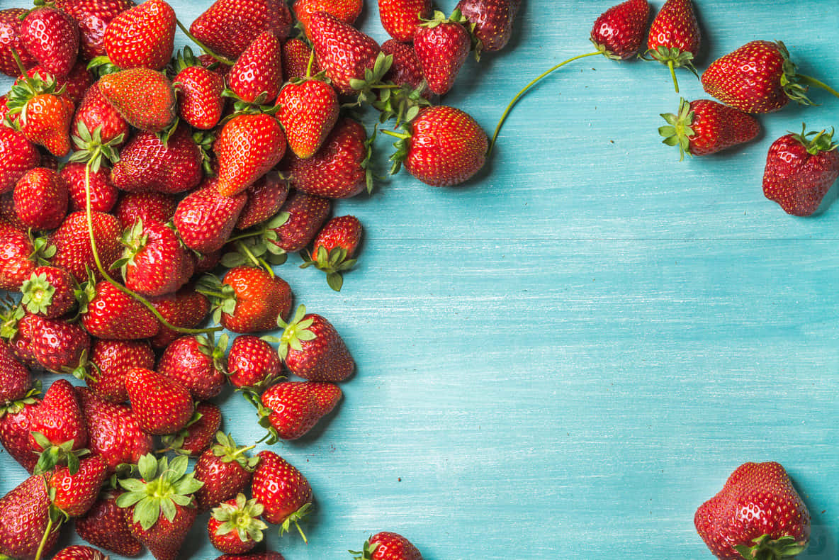 Strawberries 桌布 壁紙 — 多汁成熟的草莓散落在充滿活力的藍綠色木質表面上，俯拍平鋪構圖。