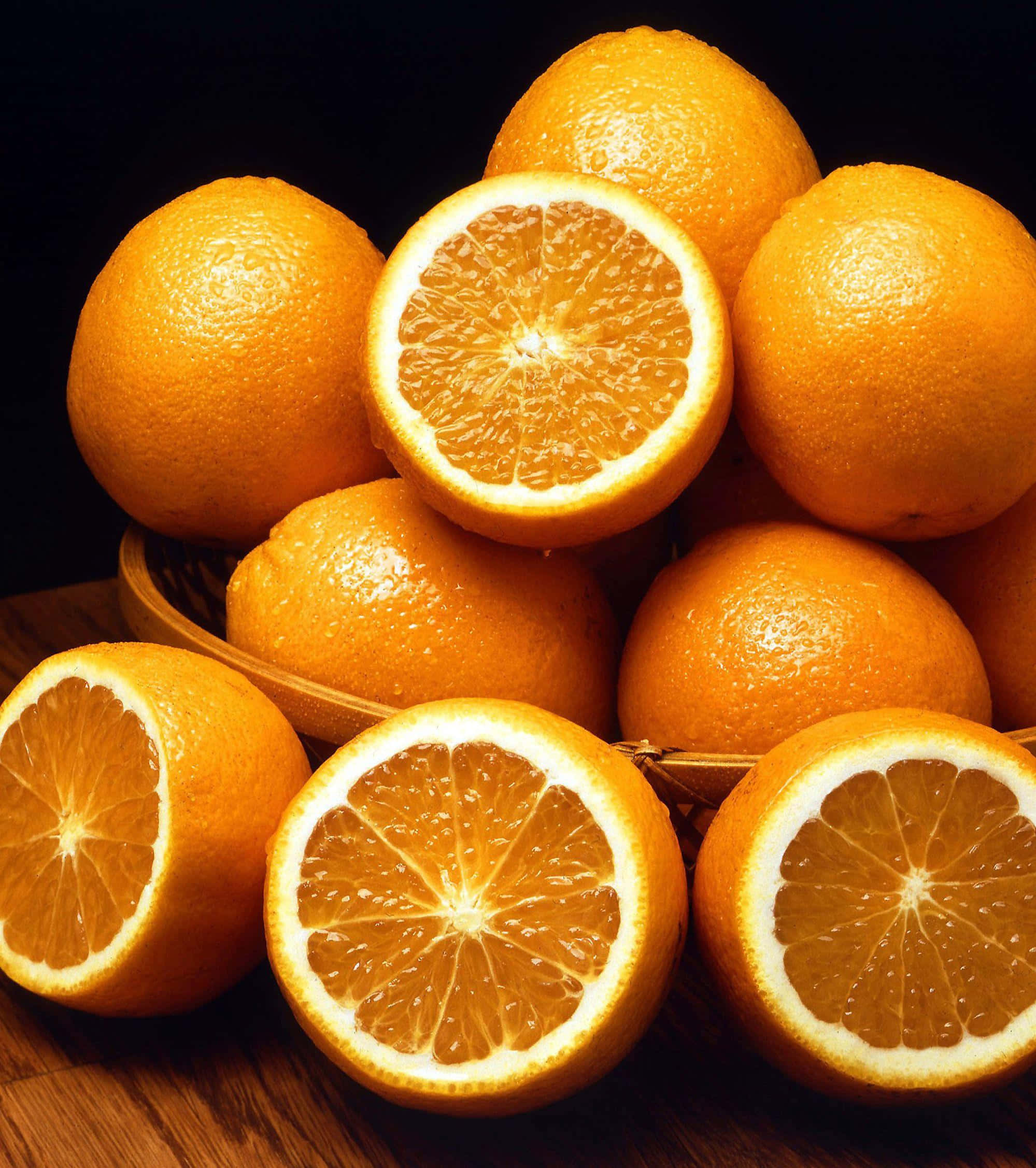 Orange Fruit 桌布 壁紙 — 多汁柳橙切開，露出鮮豔的橙瓣，堆疊在編織籃中，背景深色。