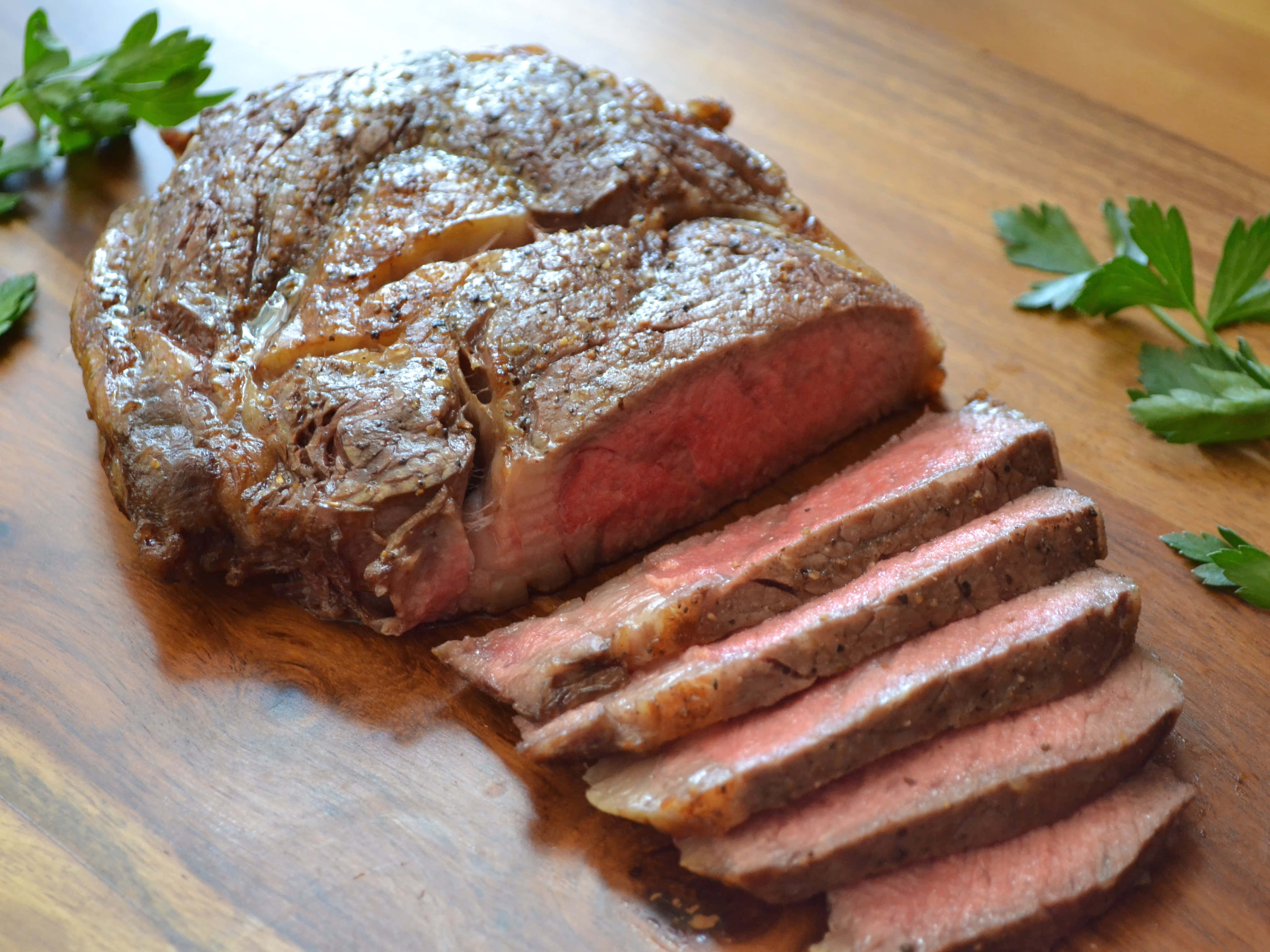 肉 桌布 壁紙 — 多汁的 medium-rare 烤牛肉，切片露出粉紅色中心，放在木砧板上，飾以新鮮歐芹。