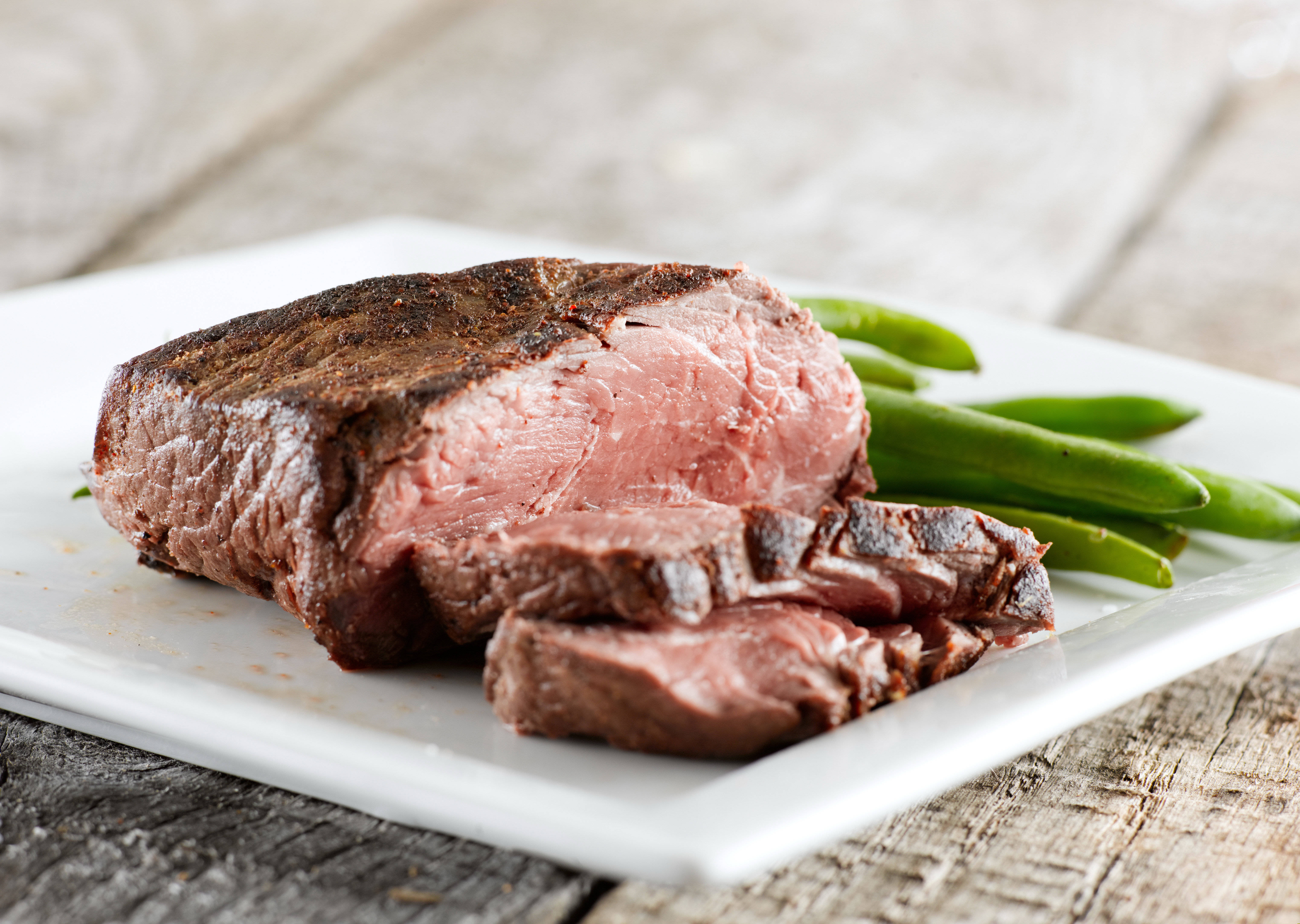 meat 桌布 壁紙 — 多汁的 medium-rare 牛排搭配青豆，盛放在白色盤子上，置於樸實的木桌上。