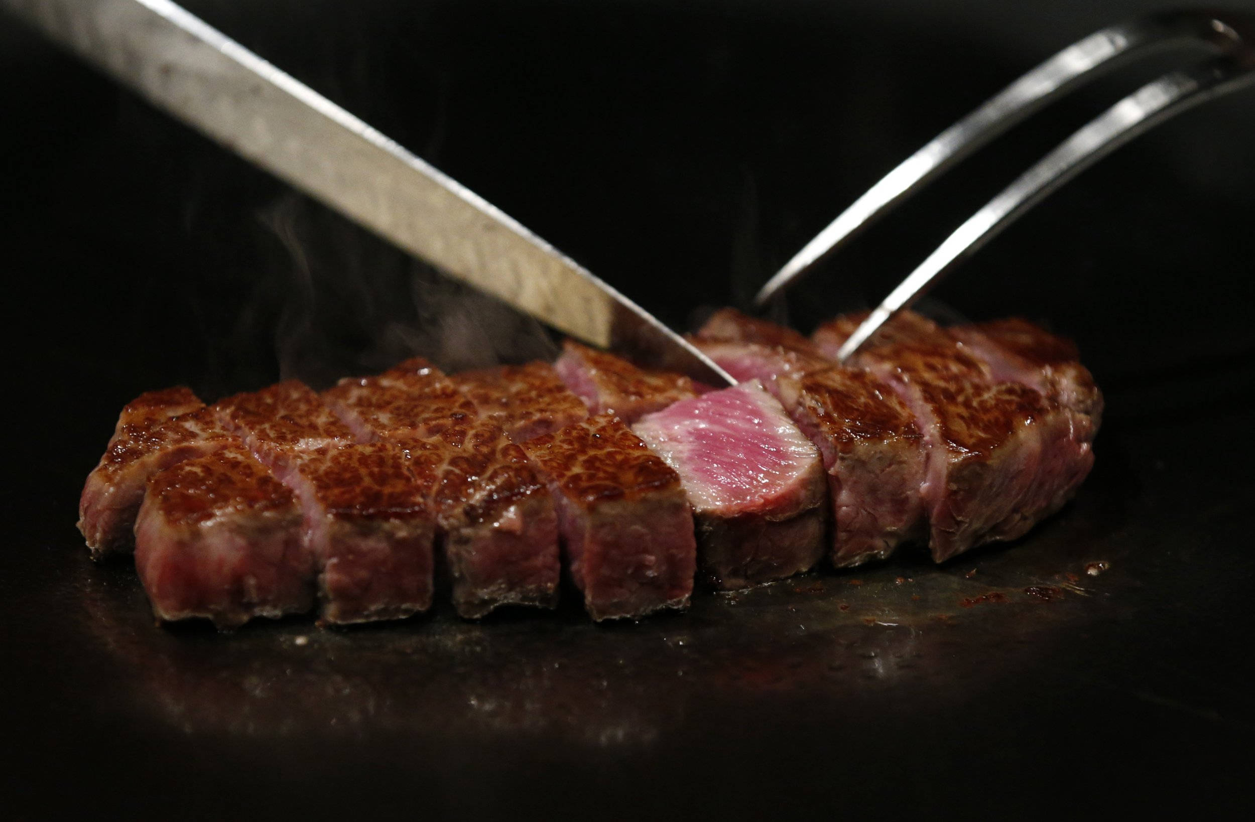 meat 桌布 壁紙 — 多汁的 medium-rare 牛排正在熱烤盤上滋滋作響，刀叉切開完美烤焦的外皮。