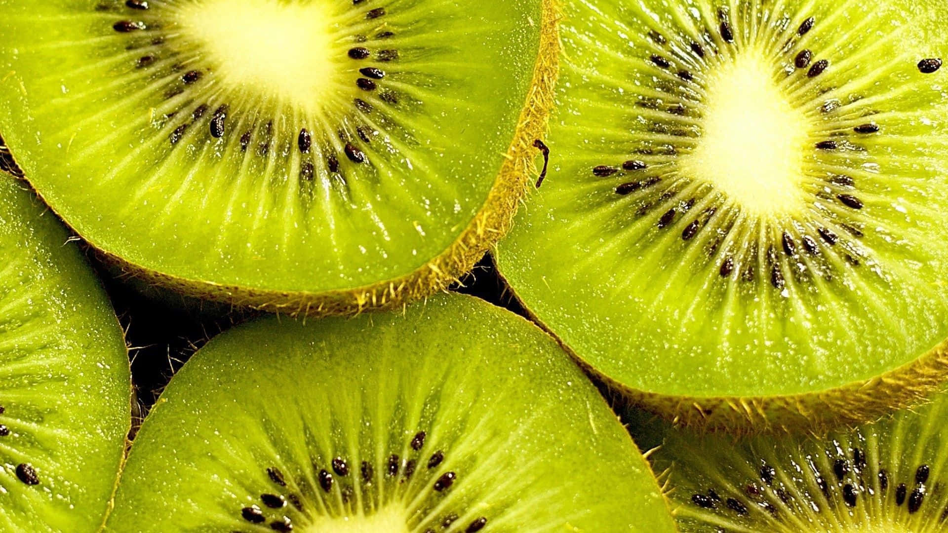 Kiwi 桌布 壁紙 — 多汁的切片奇異果，帶有鮮綠色的果肉和黑色的種子，在明亮的光線下閃閃發光。