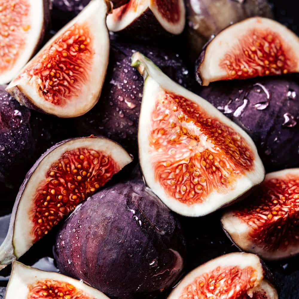 Purple Figs 桌布 壁紙 — 多汁的切片無花果，鮮紅色果肉和金色種子在深紫色果皮上閃爍著水珠。