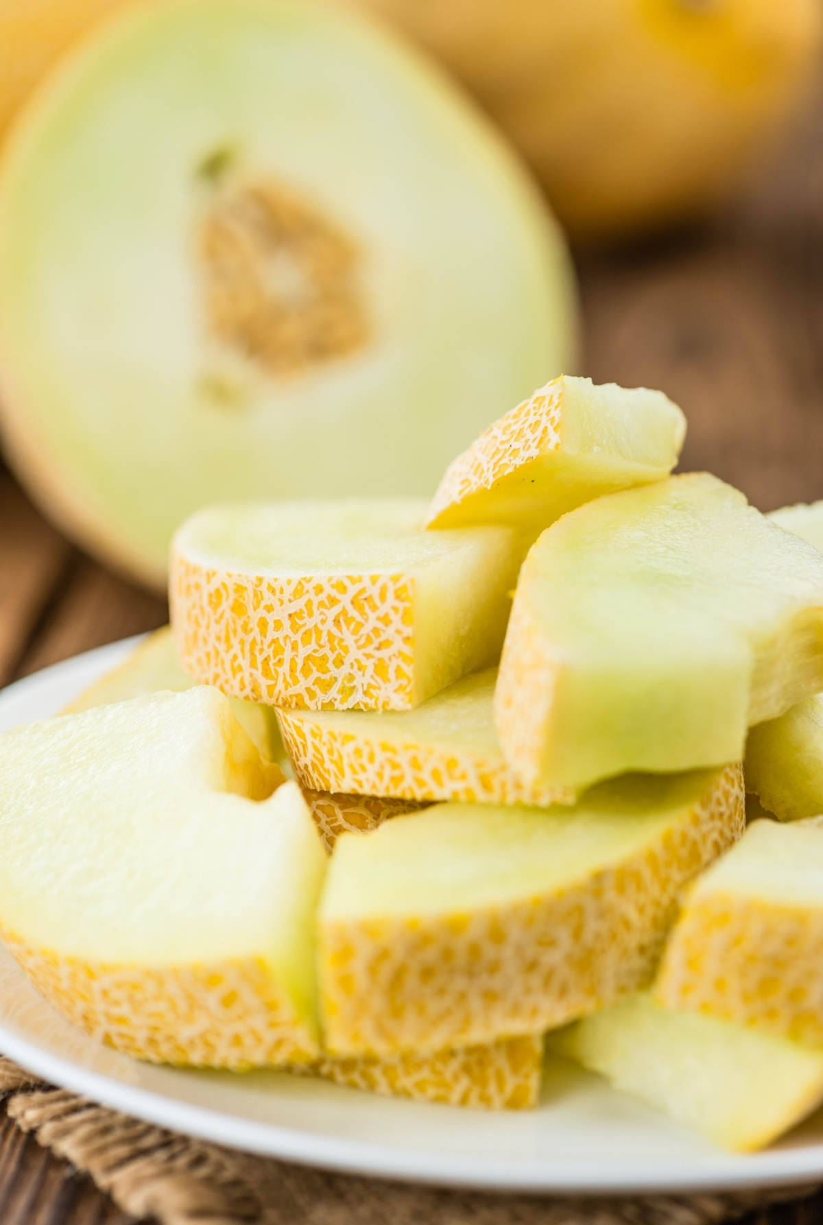 Fruits 桌布 壁紙 — 多汁的哈密瓜片堆疊在白色盤子上，後方木質表面有半個哈密瓜柔焦效果。