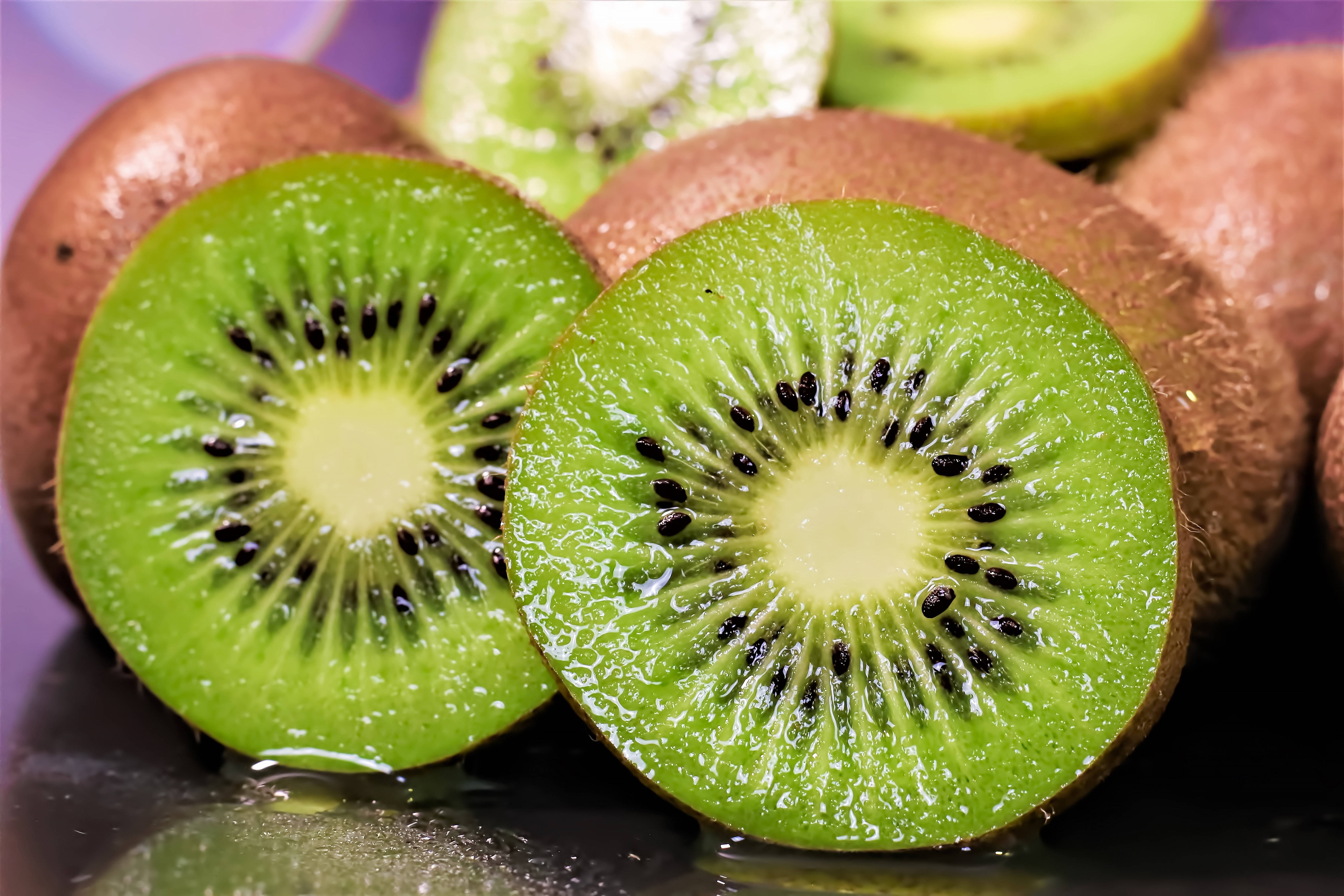 Kiwi 桌布 壁紙 — 多汁的奇異果切片，帶有鮮綠色果肉和黑色種子，在深色反光表面上閃閃發光。