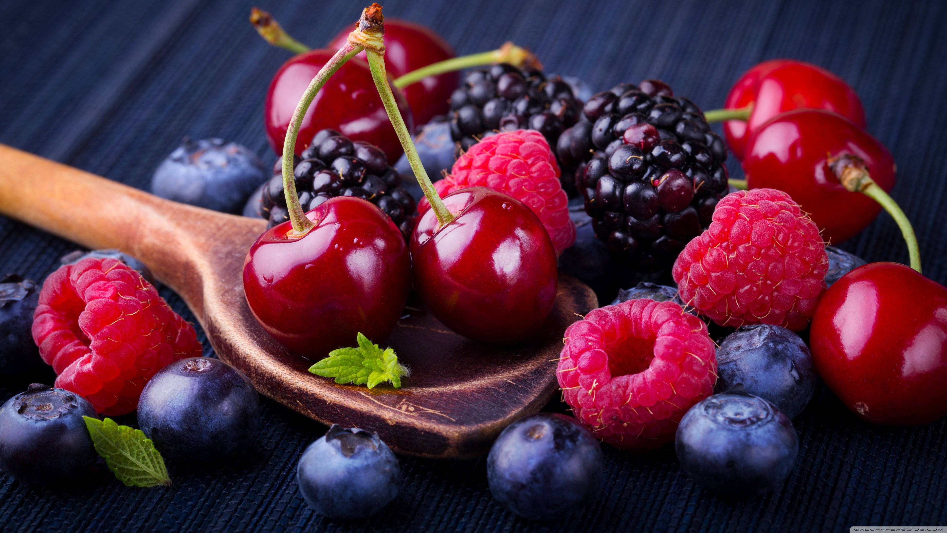 Fruit 桌布 壁紙 — 多汁的櫻桃、覆盆子、黑莓和藍莓在木匙上閃閃發光，背景為深色紋理。