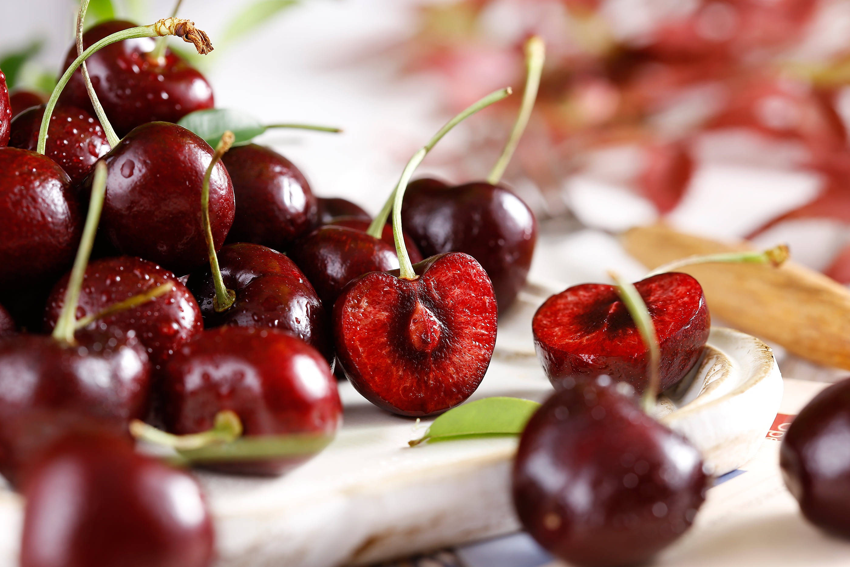 Cherry 桌布 壁紙 — 多汁的深紅色櫻桃在大理石表面上閃爍著露珠，背景是模糊的花卉。