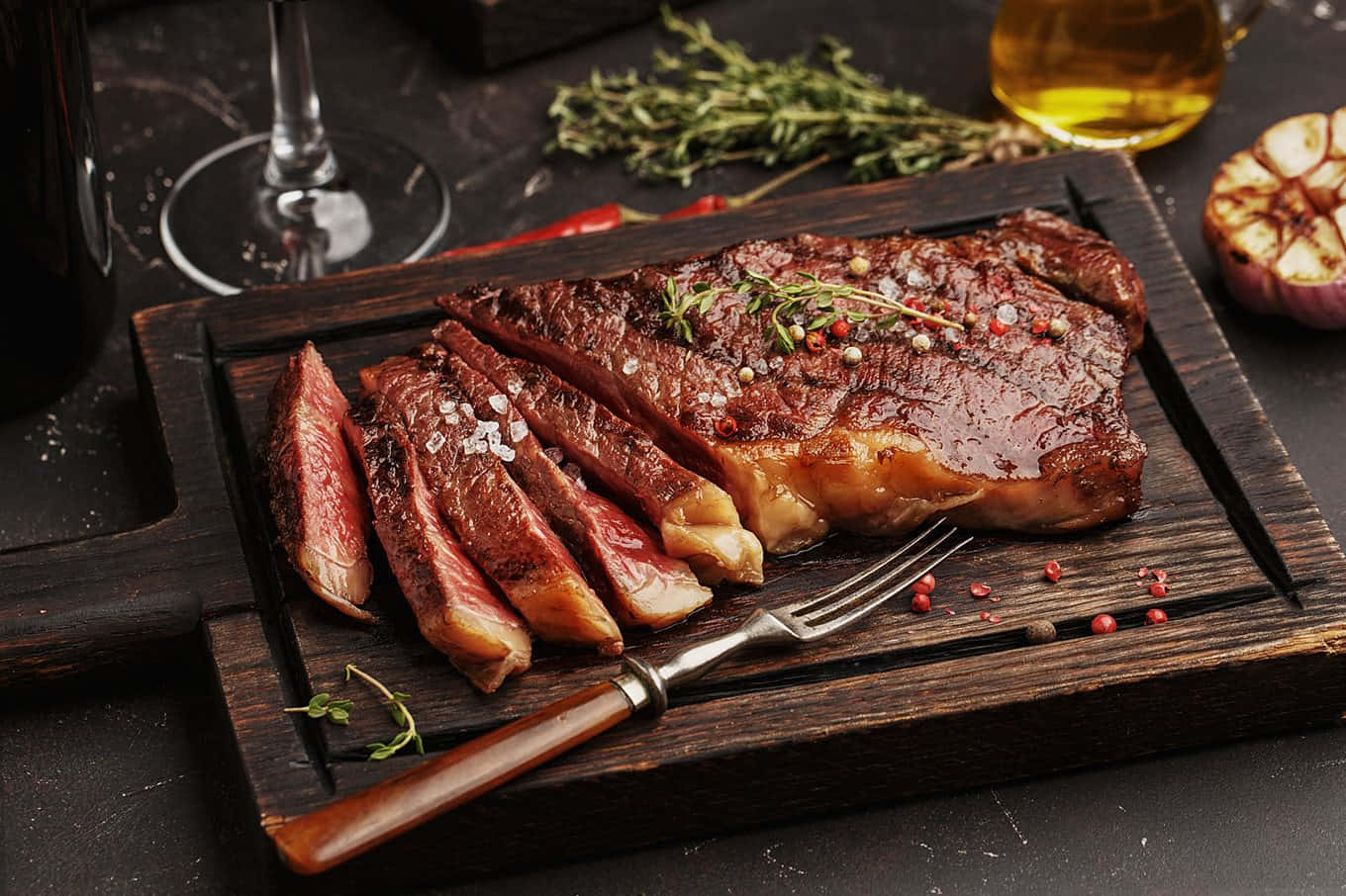 meat 桌布 壁紙 — 多汁的烤牛排切片放在質樸的木板上，搭配香草、鹽和烤大蒜，旁邊放著一杯葡萄酒。