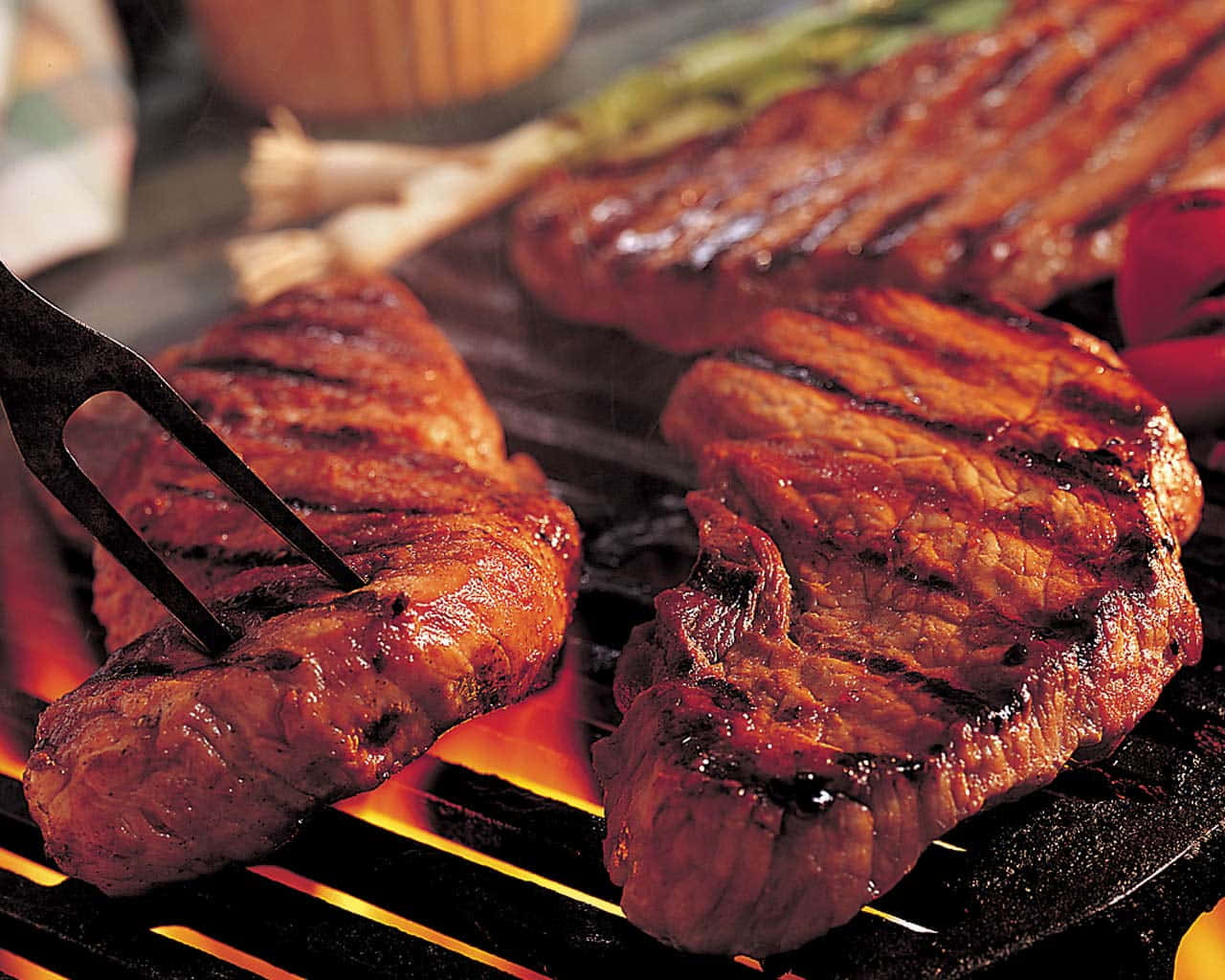 Steak 桌布 壁紙 — 多汁的烤牛排熾熱的炭火上嘶嘶作響，帶有烤痕，叉子插住一塊牛排。
