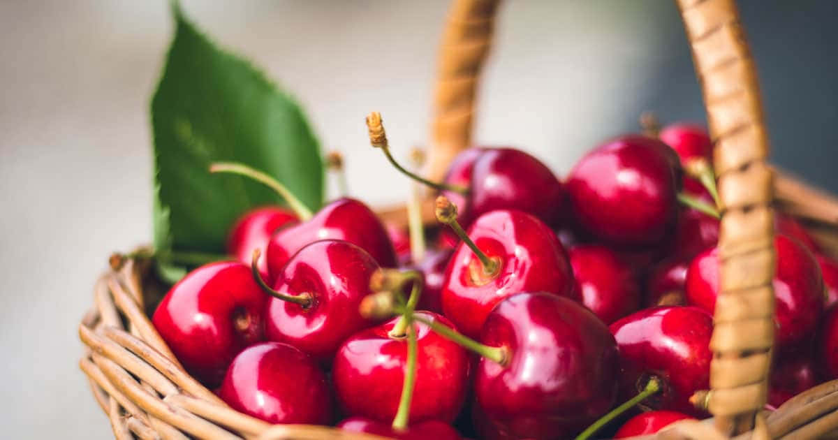 Red Cherries 桌布 壁紙 — 多汁的紅櫻桃在編織籃中閃閃發光，一片綠葉增添了新鮮感。