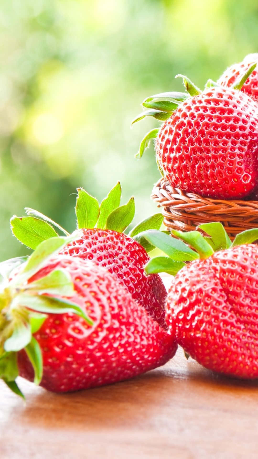 Cute Strawberry 桌布 壁紙 — 多汁的紅色草莓連同綠色葉子放在木質表面上，旁邊有一個小編織籃。