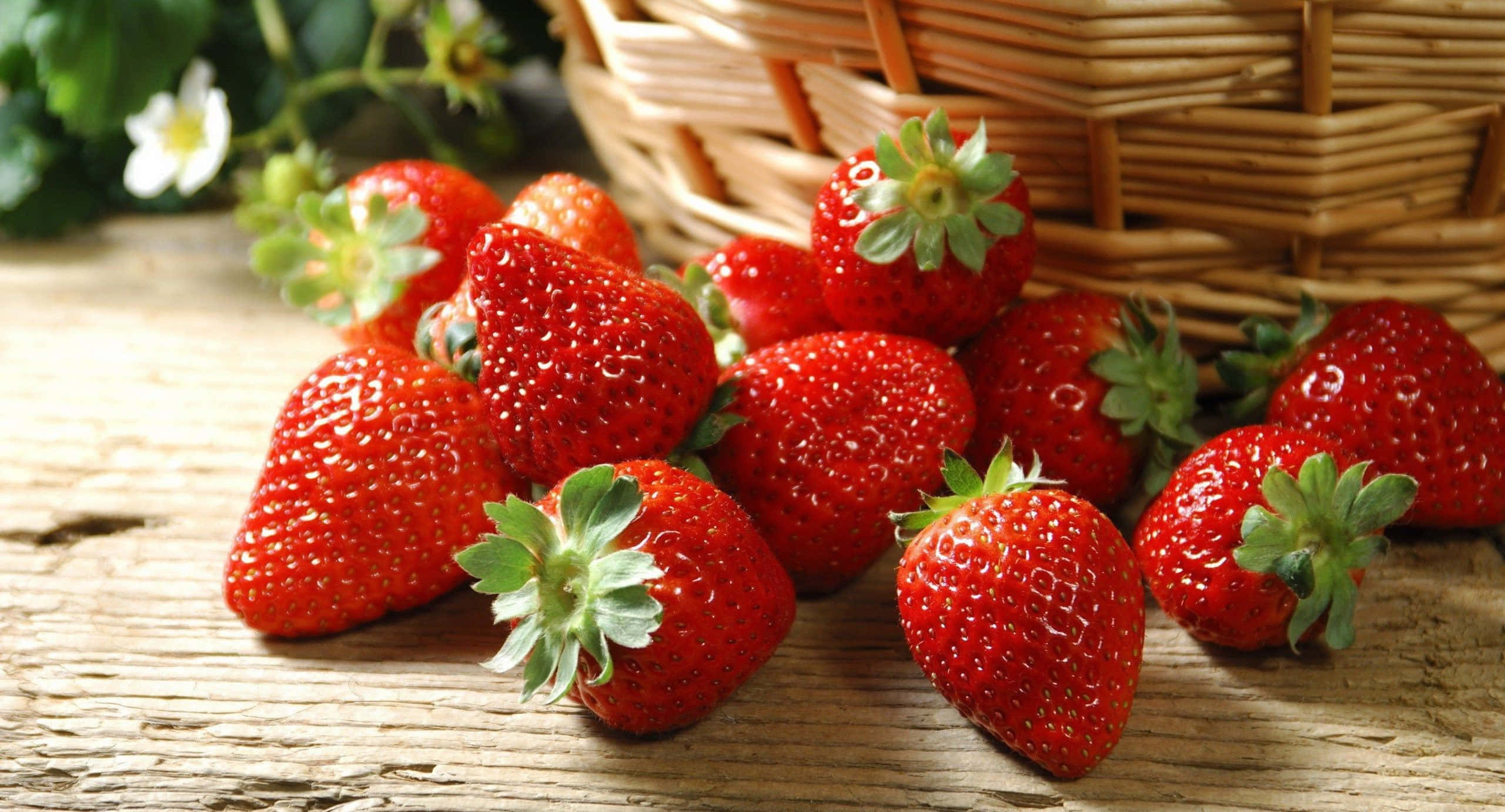 Red Strawberry 桌布 壁紙 — 多汁的紅色草莓連著綠色蒂頭從編織籃子裡溢出，落在質樸的木質表面上。