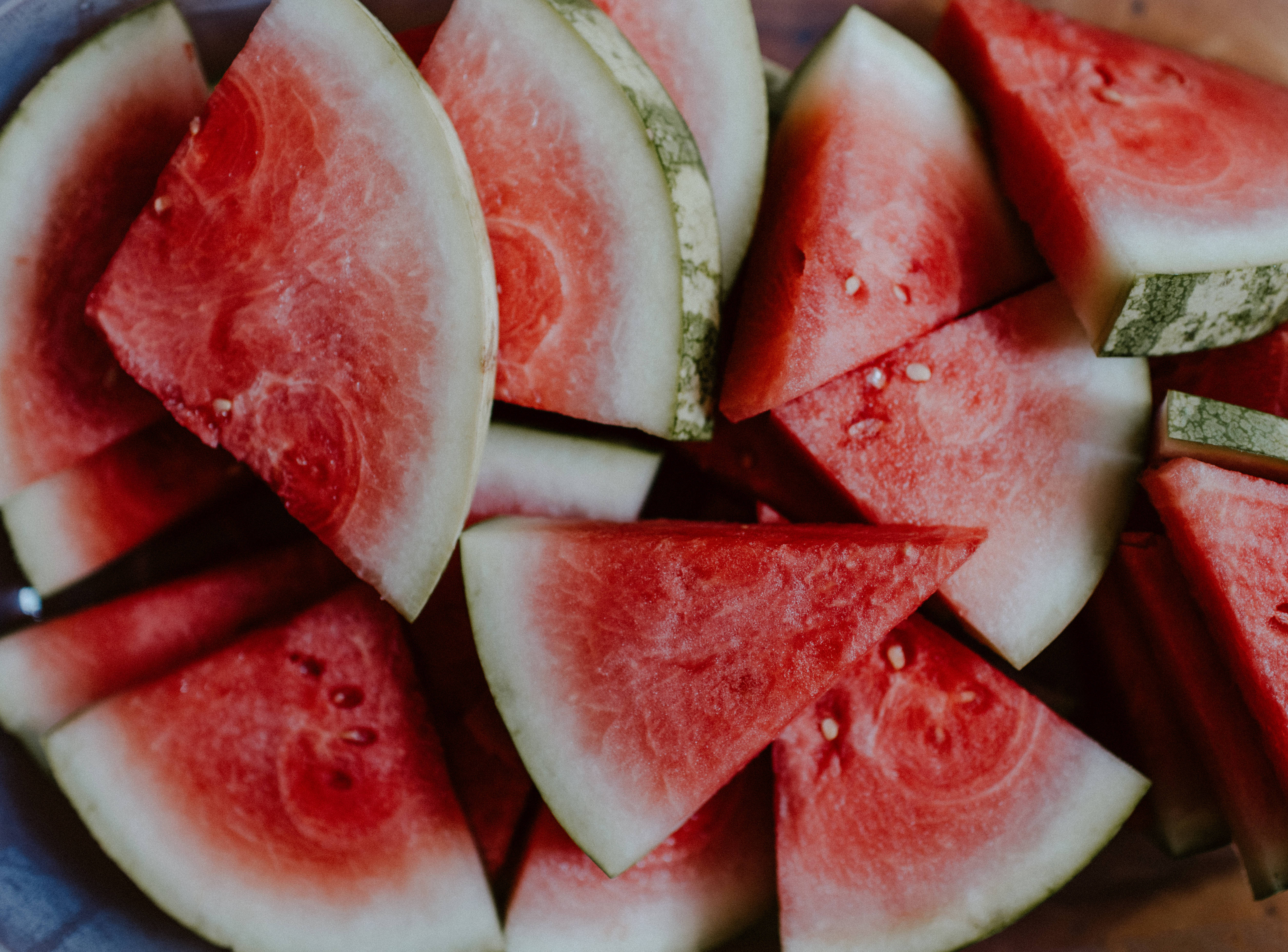 Watermelon 桌布 壁紙 — 多汁的紅色西瓜片，帶有白色瓜皮和黑色種子，堆放在一個質樸的木碗中。