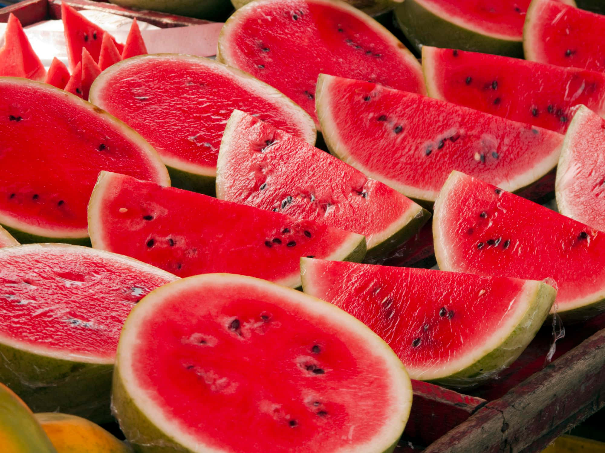 Watermelon 桌布 壁紙 — 多汁的紅色西瓜片，帶有黑色種子，排列在充滿活力、陽光明媚的市場展示中。