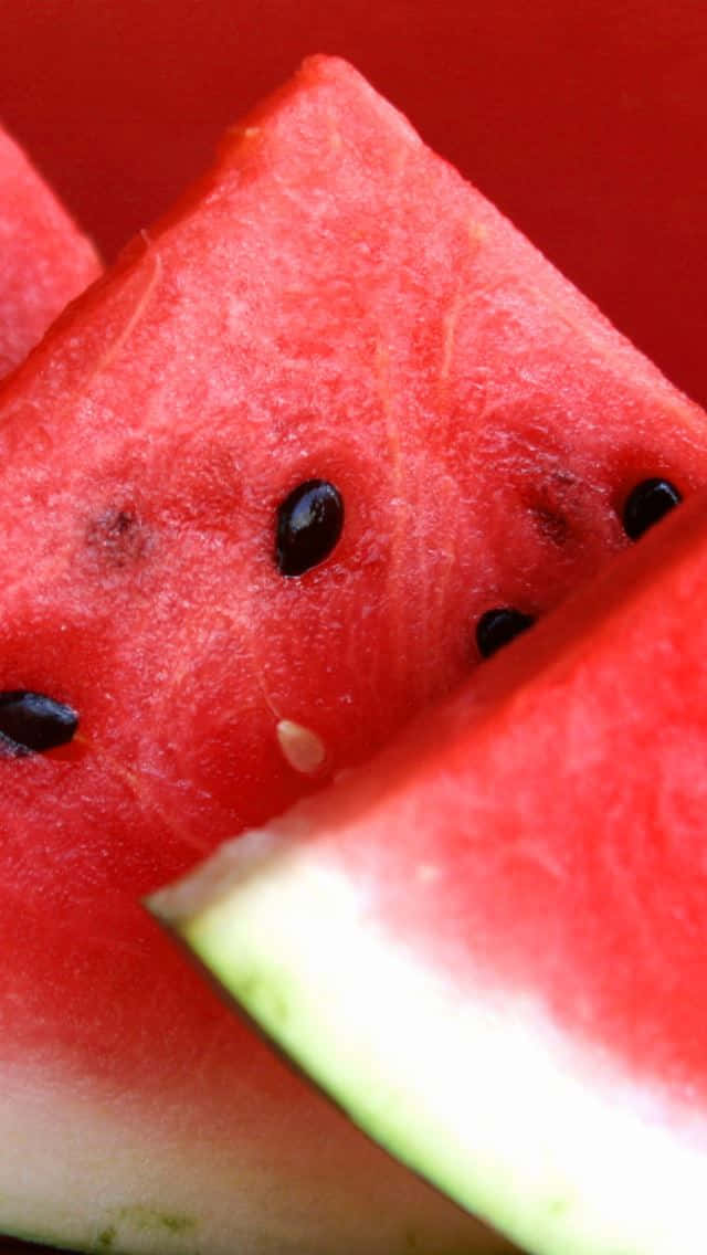 Watermelon iPhone 桌布 壁紙 — 多汁的紅色西瓜片，帶有黑色種子和淡色外皮，背景為深紅色。