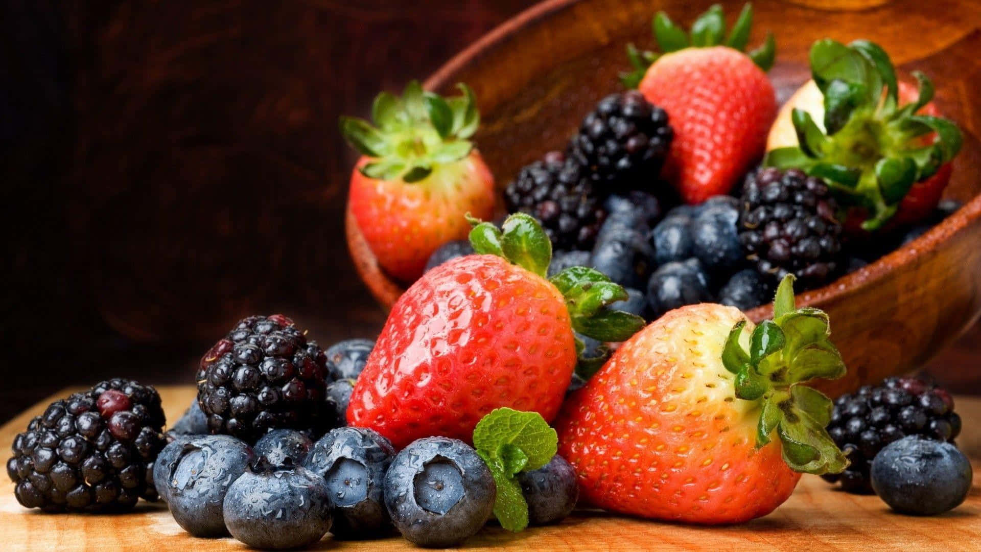 Healthy Food 桌布 壁紙 — 多汁的草莓、藍莓和黑莓在溫暖的木質表面上的質樸木碗中閃爍著露珠。
