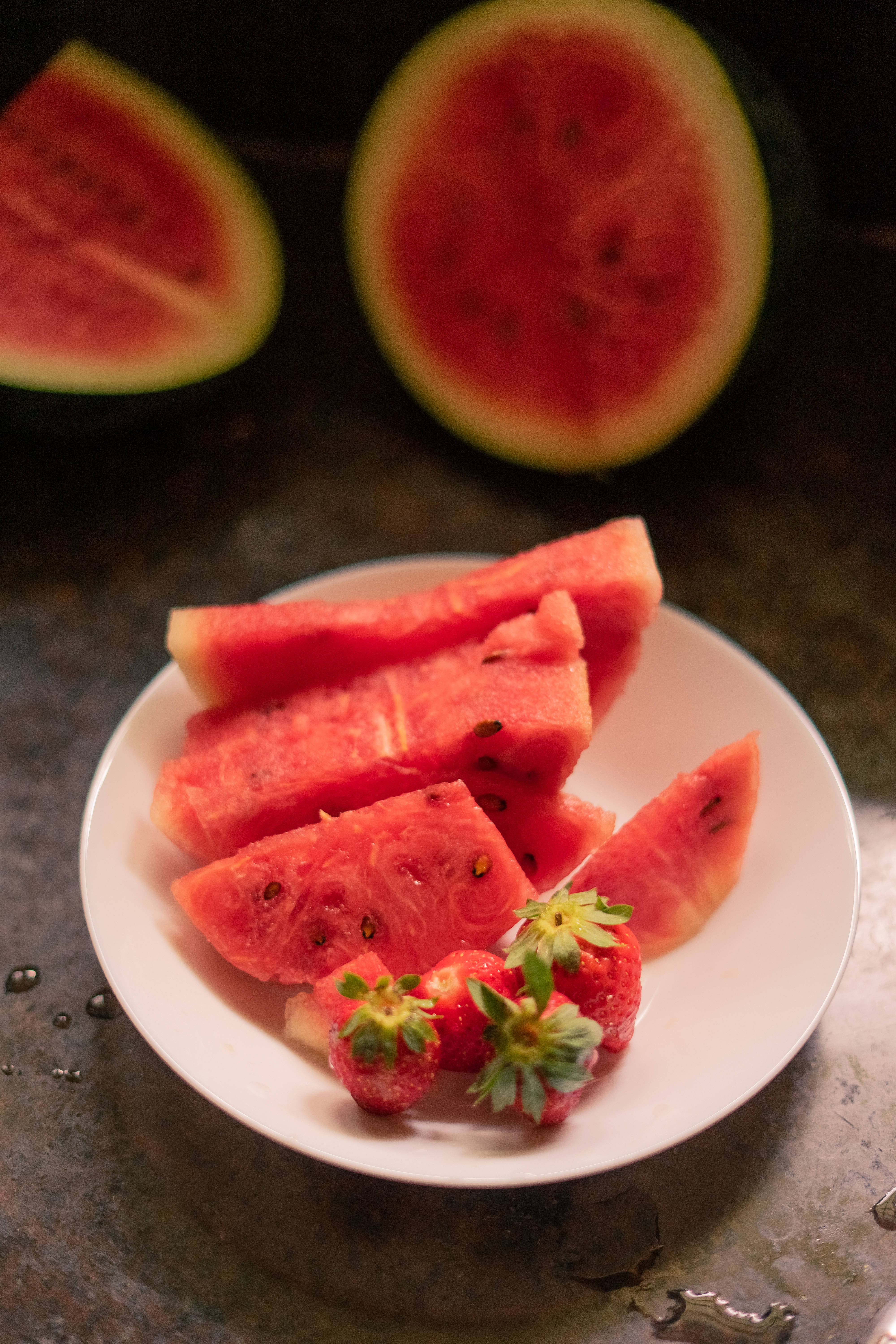 Watermelon 桌布 壁紙 — 多汁的西瓜片和新鮮草莓放在白色盤子上，背景為深色紋理。
