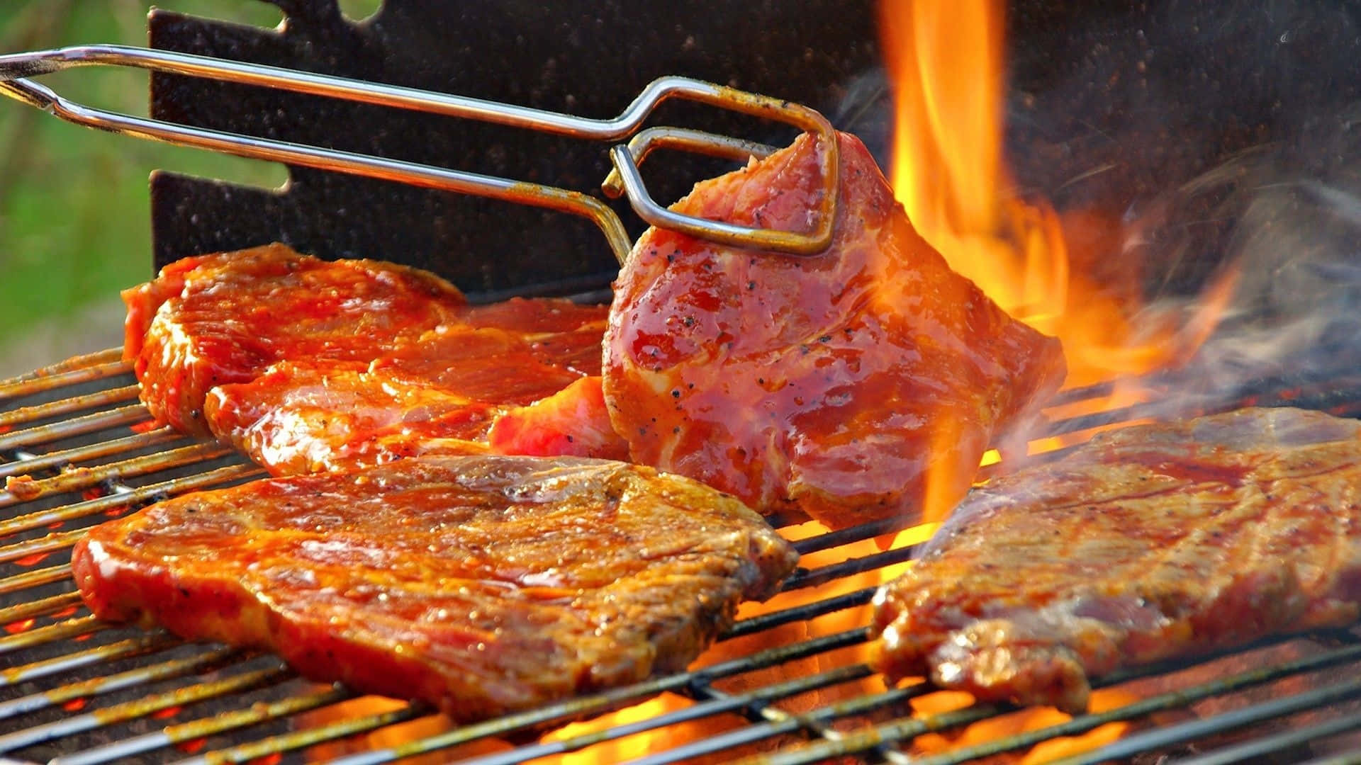 Bbq 桌布 壁紙 — 多汁的醃製牛排在大火上烤得滋滋作響，用夾子夾起一塊牛排，露出焦黑完美的狀態。