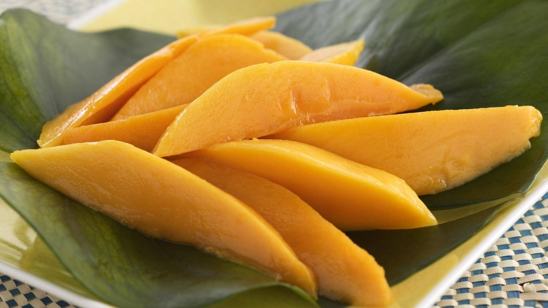 Fruit 桌布 壁紙 — 多汁的金色芒果片放在有圖案的盤子上的一片大綠葉上。