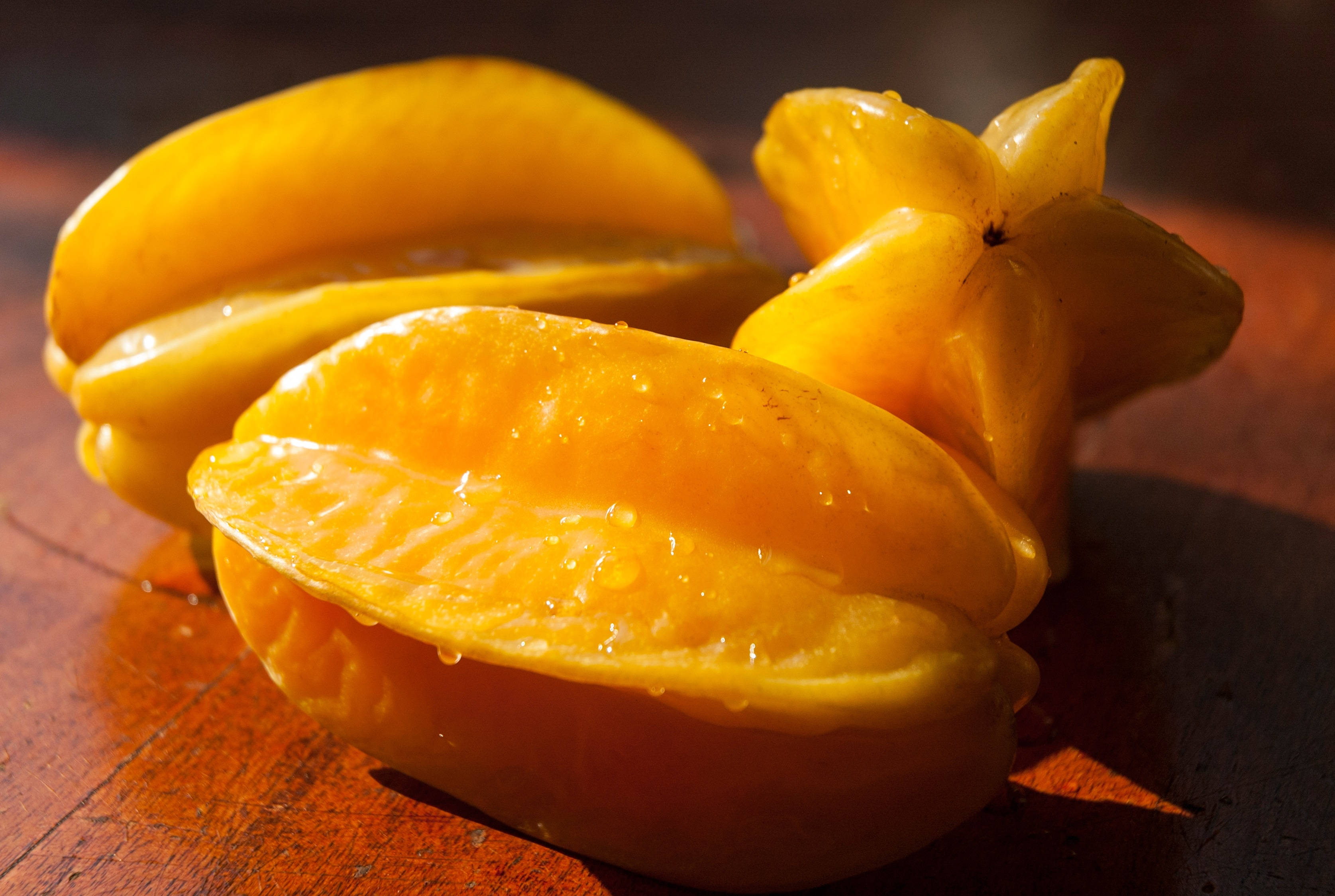 Fruit 桌布 壁紙 — 多汁的黃色楊桃在柔和的陽光下，在溫暖的木質表面上閃爍著露珠。
