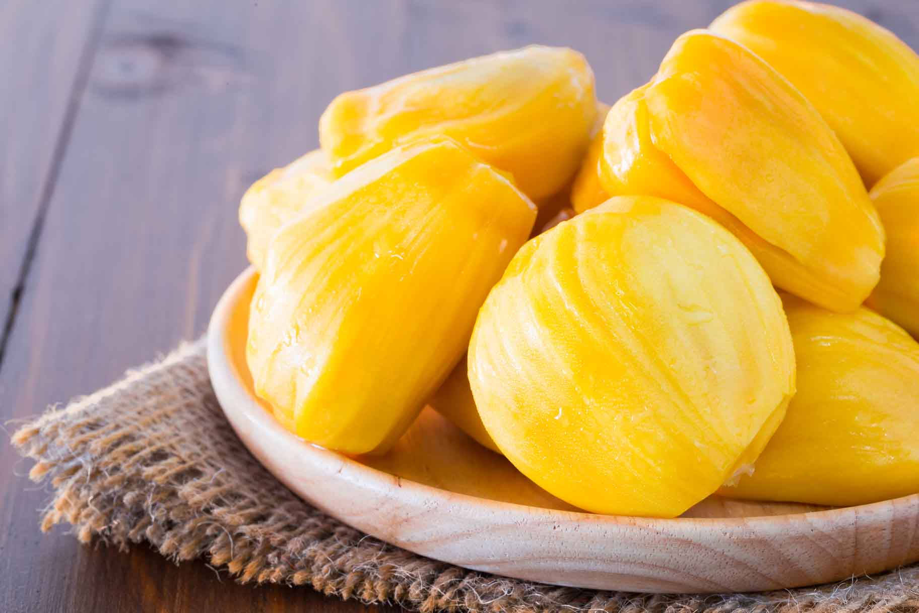 Fruit 桌布 壁紙 — 多汁的黃色波羅蜜塊在深色木質表面上的麻布上的木碗中閃閃發光。