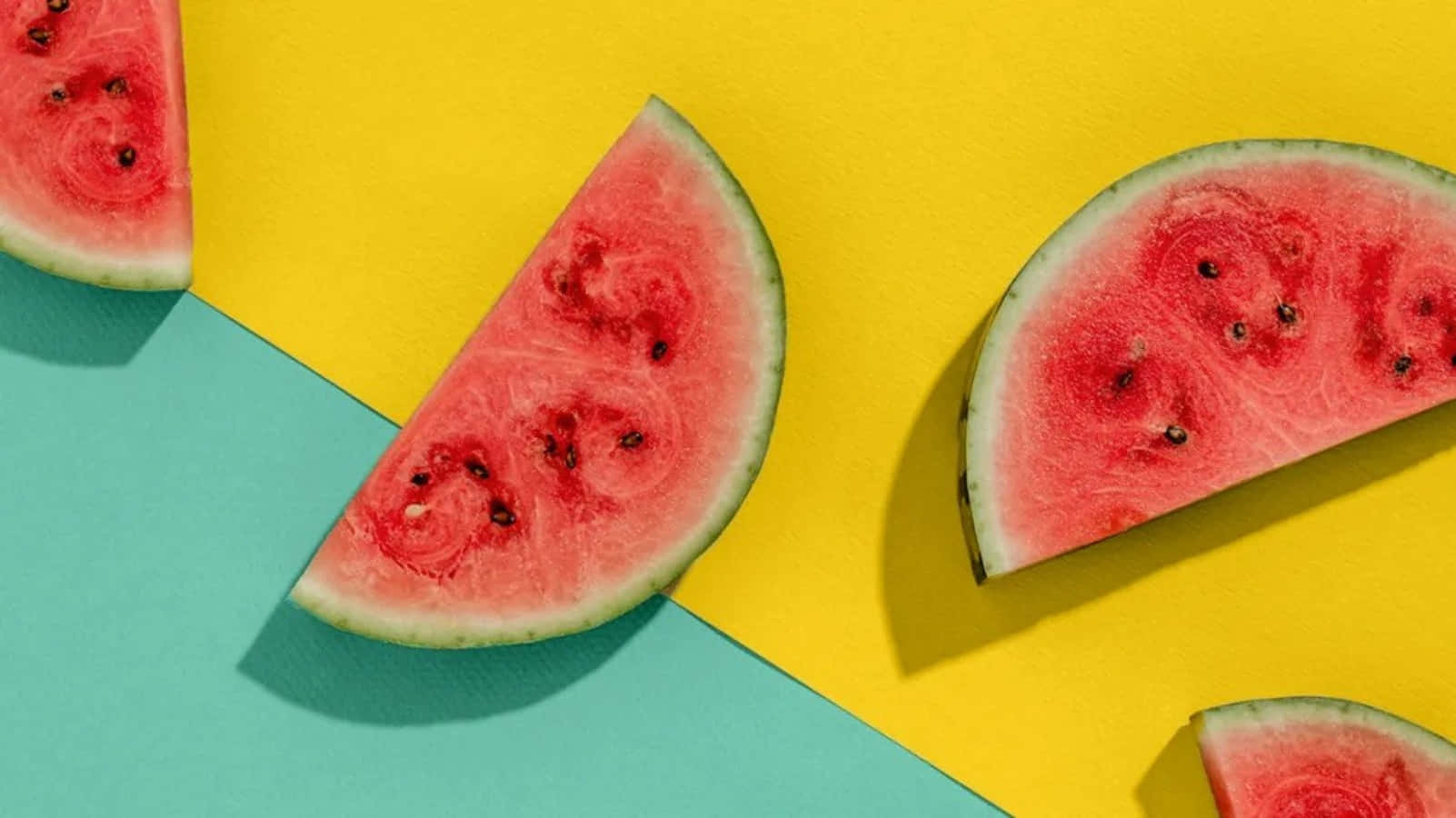 Watermelon 桌布 壁紙 — 多汁西瓜片排列在鮮明的黃色和藍綠色幾何背景上。
