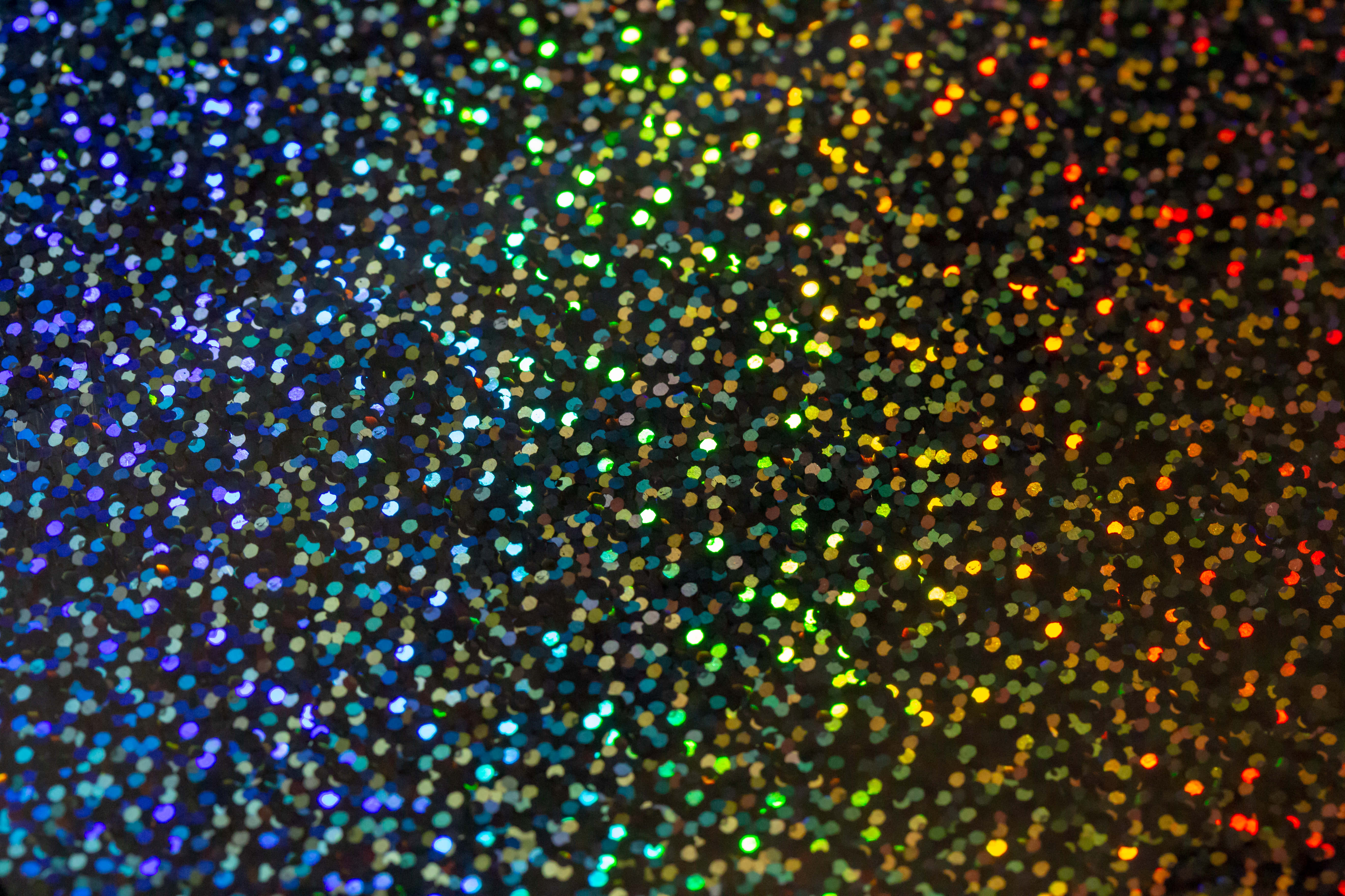 Rainbow Glitter 桌布 壁紙 — 多色閃粉粒子在深色背景上閃爍的特寫，背景從藍色漸變到橙色。