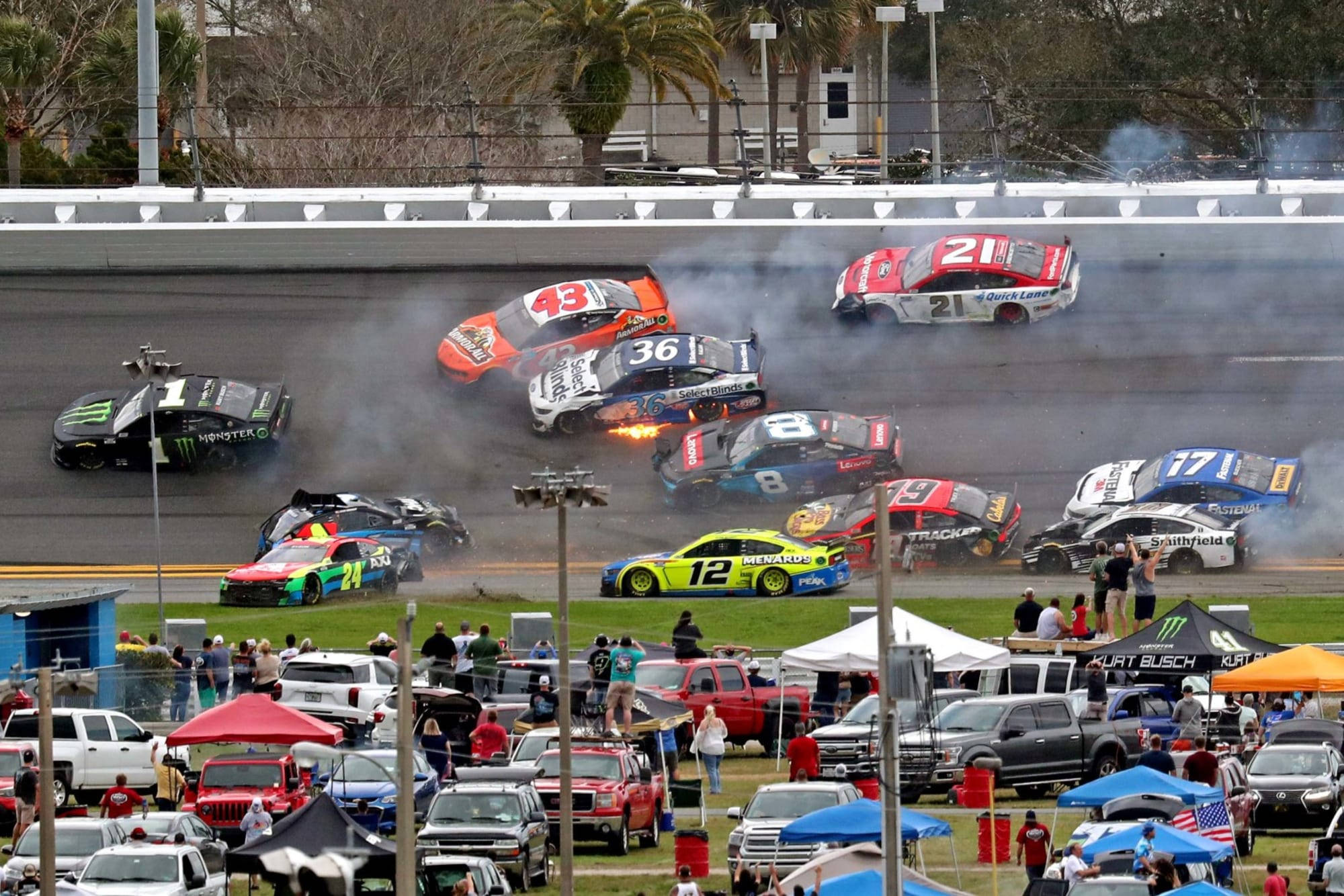 Racing 桌布 壁紙 — 多輛NASCAR賽車在賽道上猛烈相撞，冒出濃煙和火焰，觀眾從看台和攤位帳篷觀看。