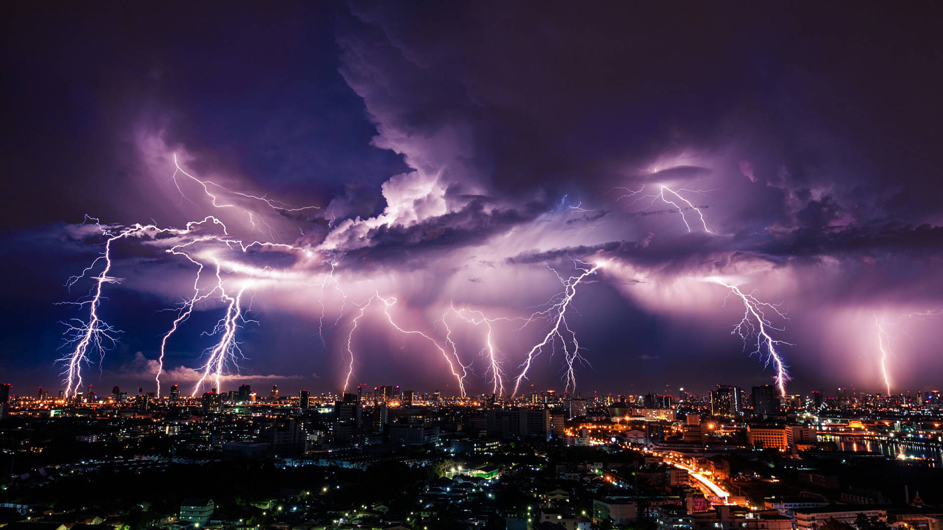 X 桌布 壁紙 — 多道鋸齒狀閃電照亮了夜晚暴風雨紫色天空下廣闊的城市景觀。