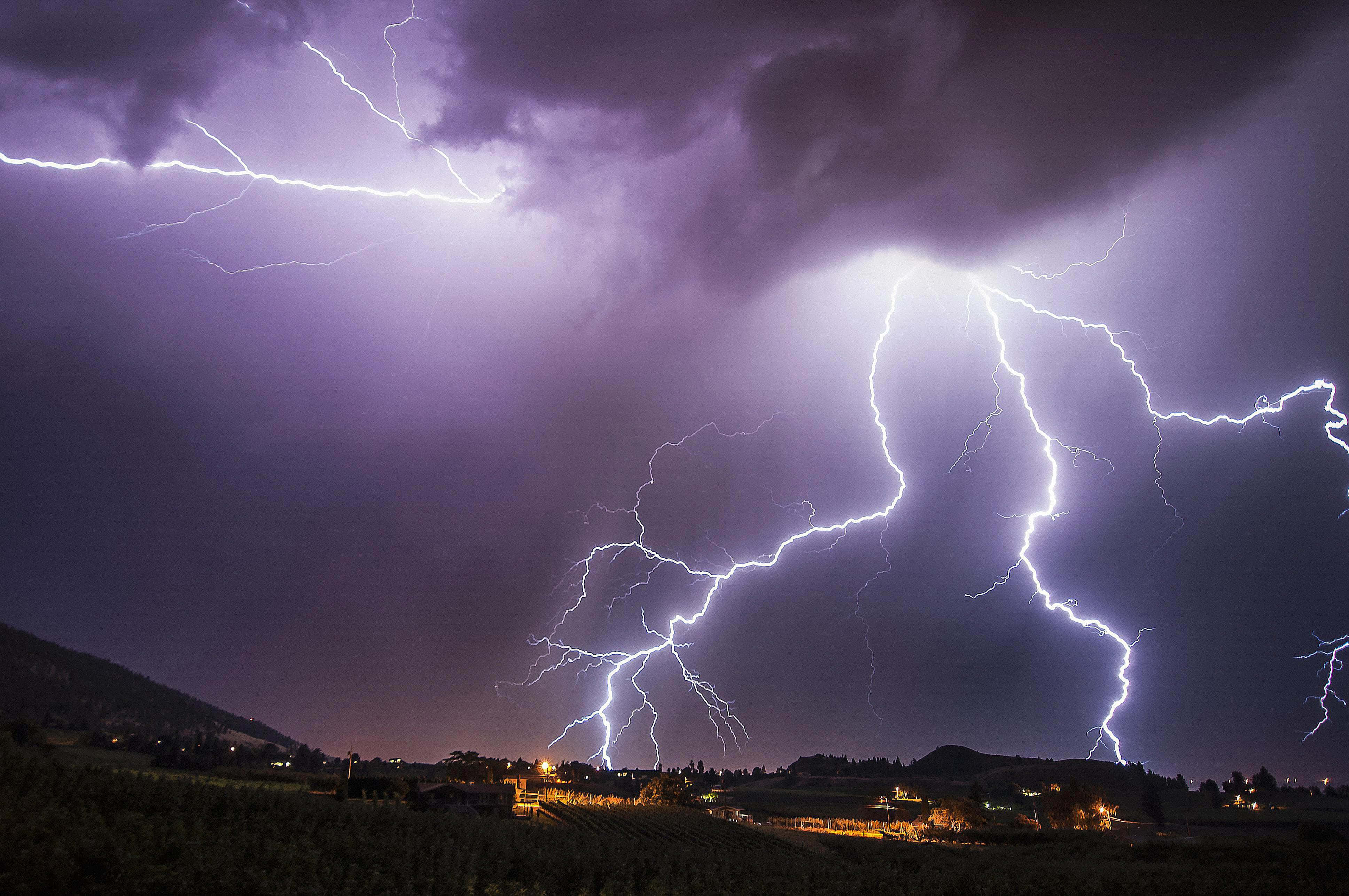 閃電 桌布 壁紙 — 多道鋸齒狀閃電照亮了夜晚鄉村景觀上方的深紫色暴風雨天空。