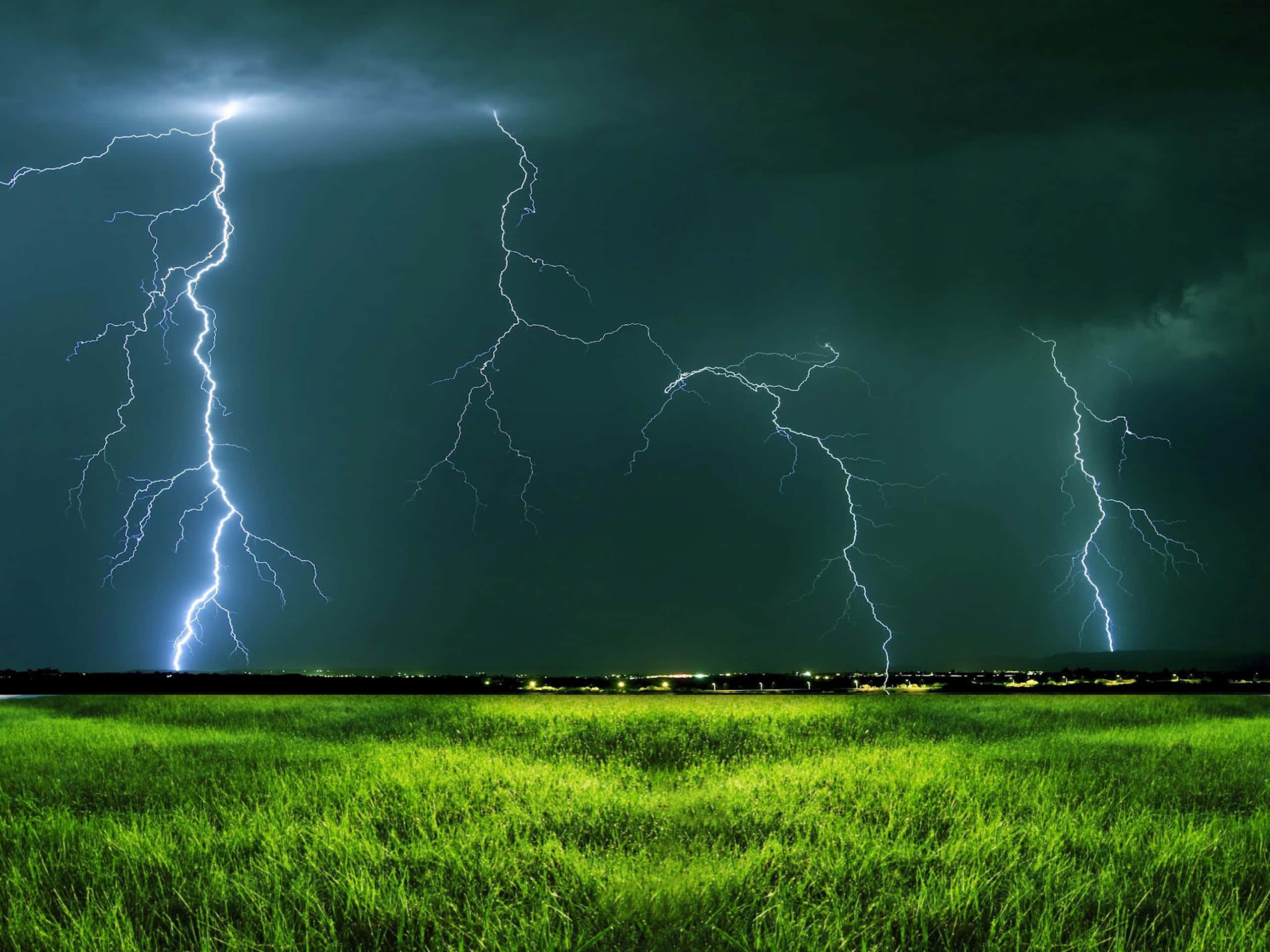 閃電 桌布 壁紙 — 多道鋸齒狀閃電照亮了夜晚黑暗暴風雨的天空下充滿活力的綠色草地。