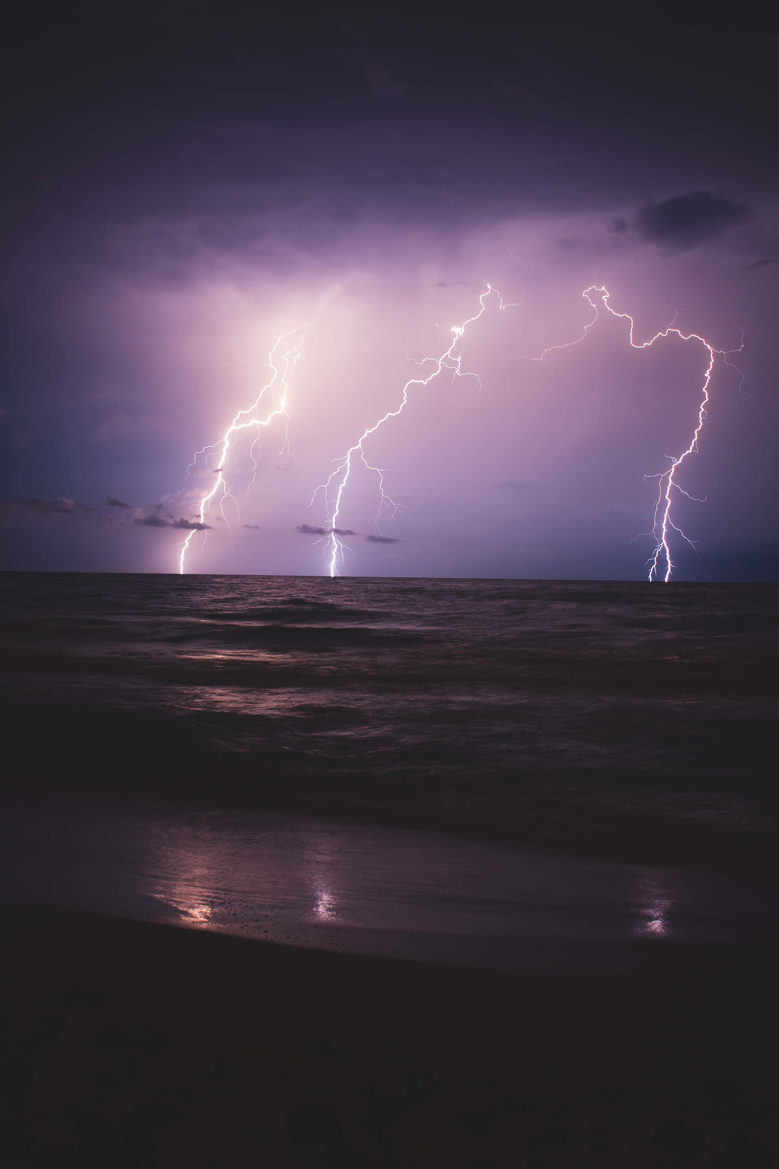 Purple Lightning 桌布 壁紙 — 多道鋸齒狀閃電照亮了夜間黑暗海洋上空暴風雨的紫色天空。