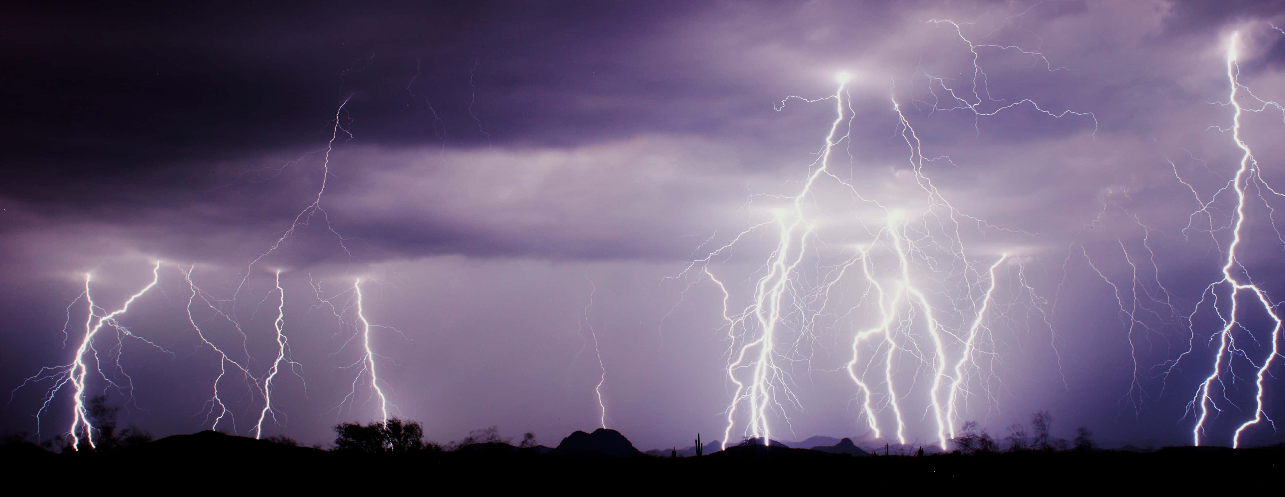 Phoenix Arizona 桌布 壁紙 — 多道鋸齒狀閃電照亮了暗紫色暴風雨天空，下方是剪影般的沙漠景觀。