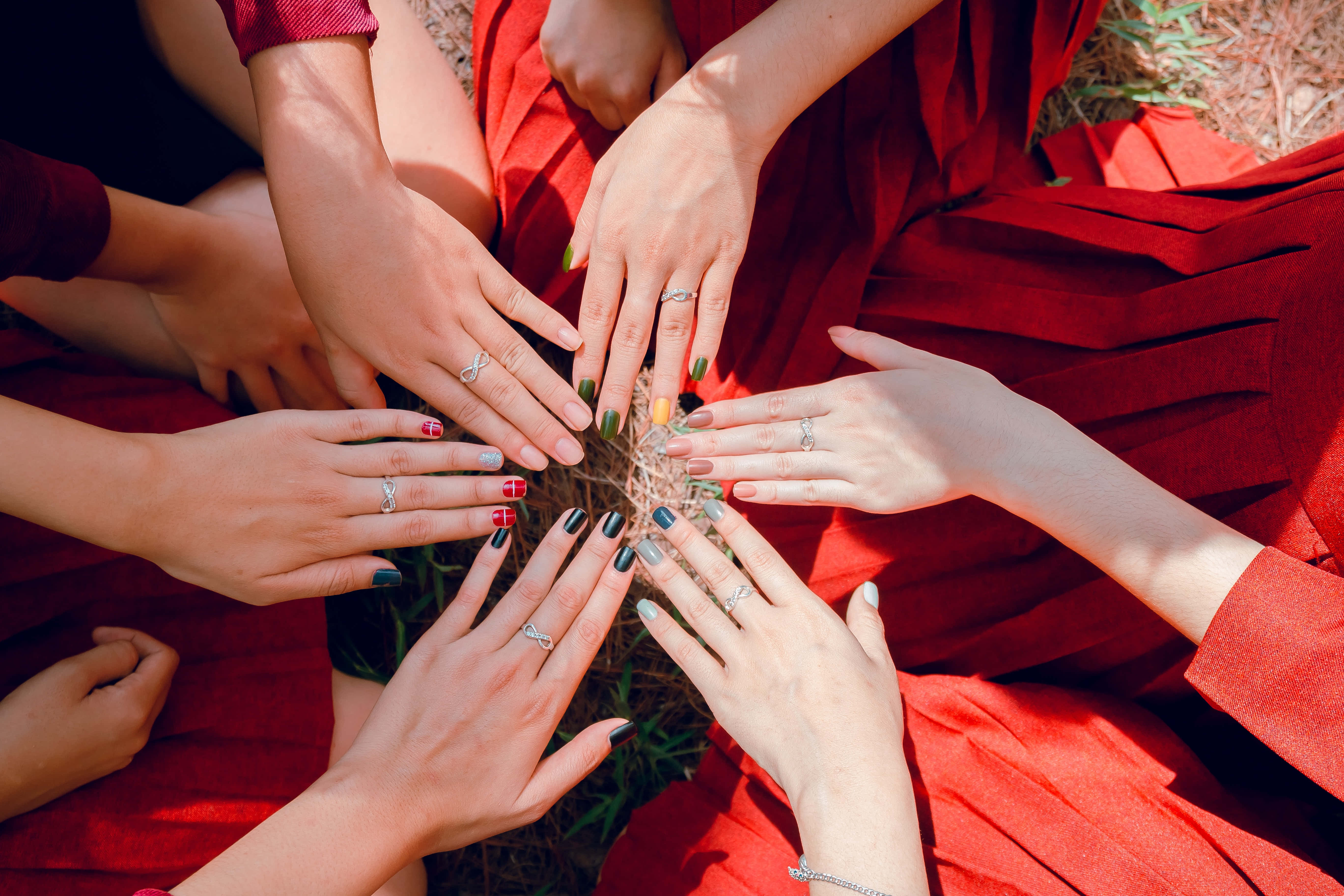 hands 桌布 壁紙 — 多隻塗有彩色指甲油和戴戒指的手在明亮的陽光下於戶外的紅色布料上圍成一個圓圈。