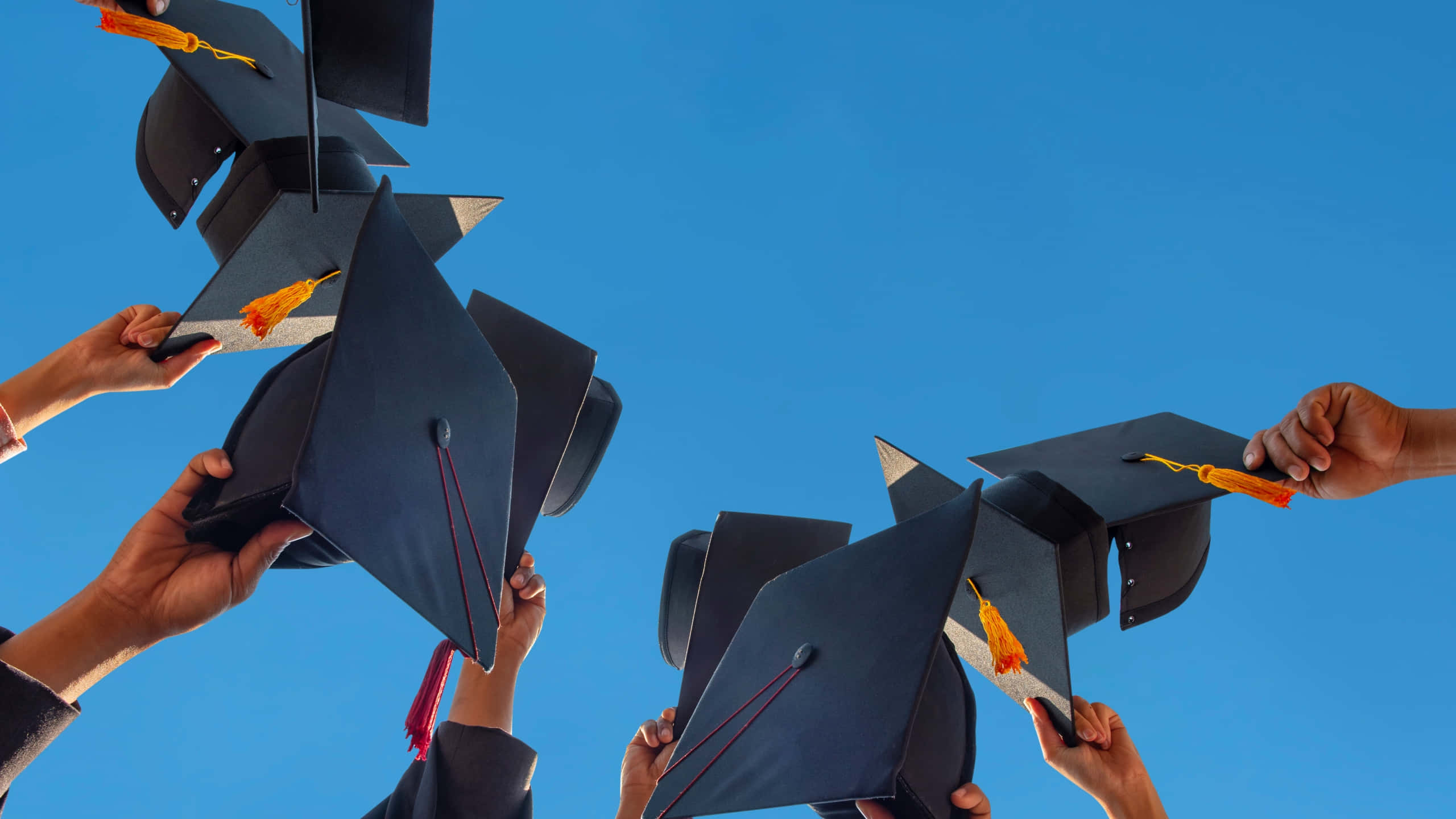 Graduation Ceremony 桌布 壁紙 — 多隻手將帶有橙色流蘇的黑色畢業帽拋向清澈的藍天。