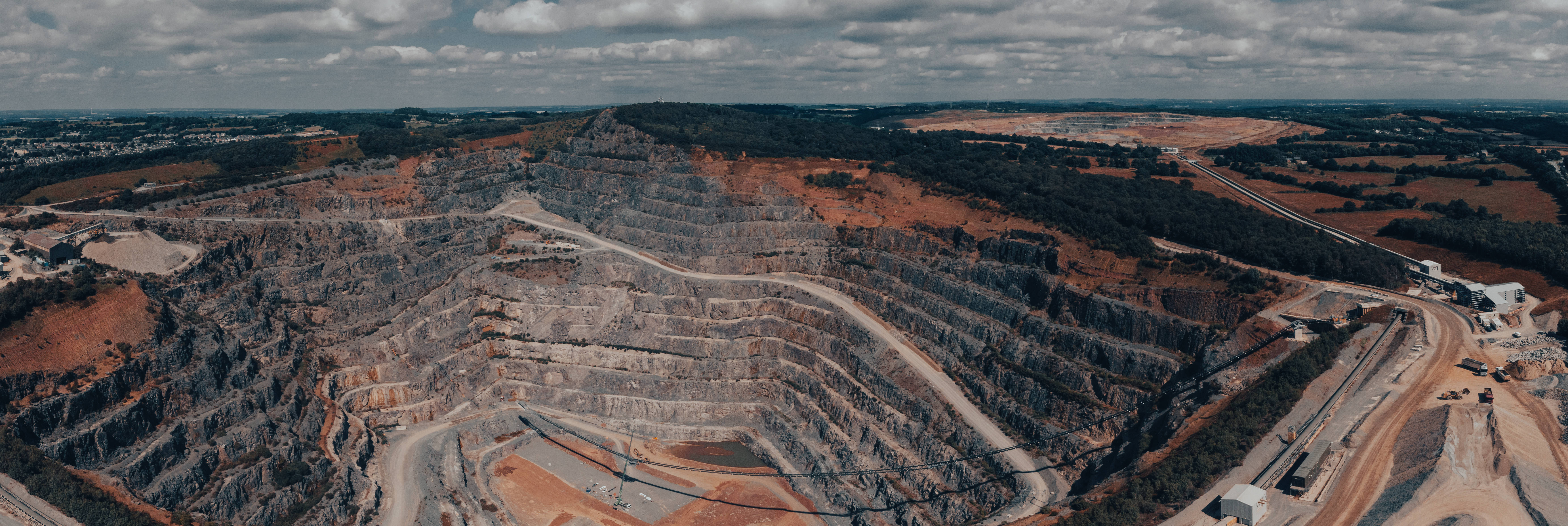 Mining 桌布 壁紙 — 多雲天空下，一個擁有梯田狀岩壁和蜿蜒道路的巨大露天礦場的鳥瞰圖。