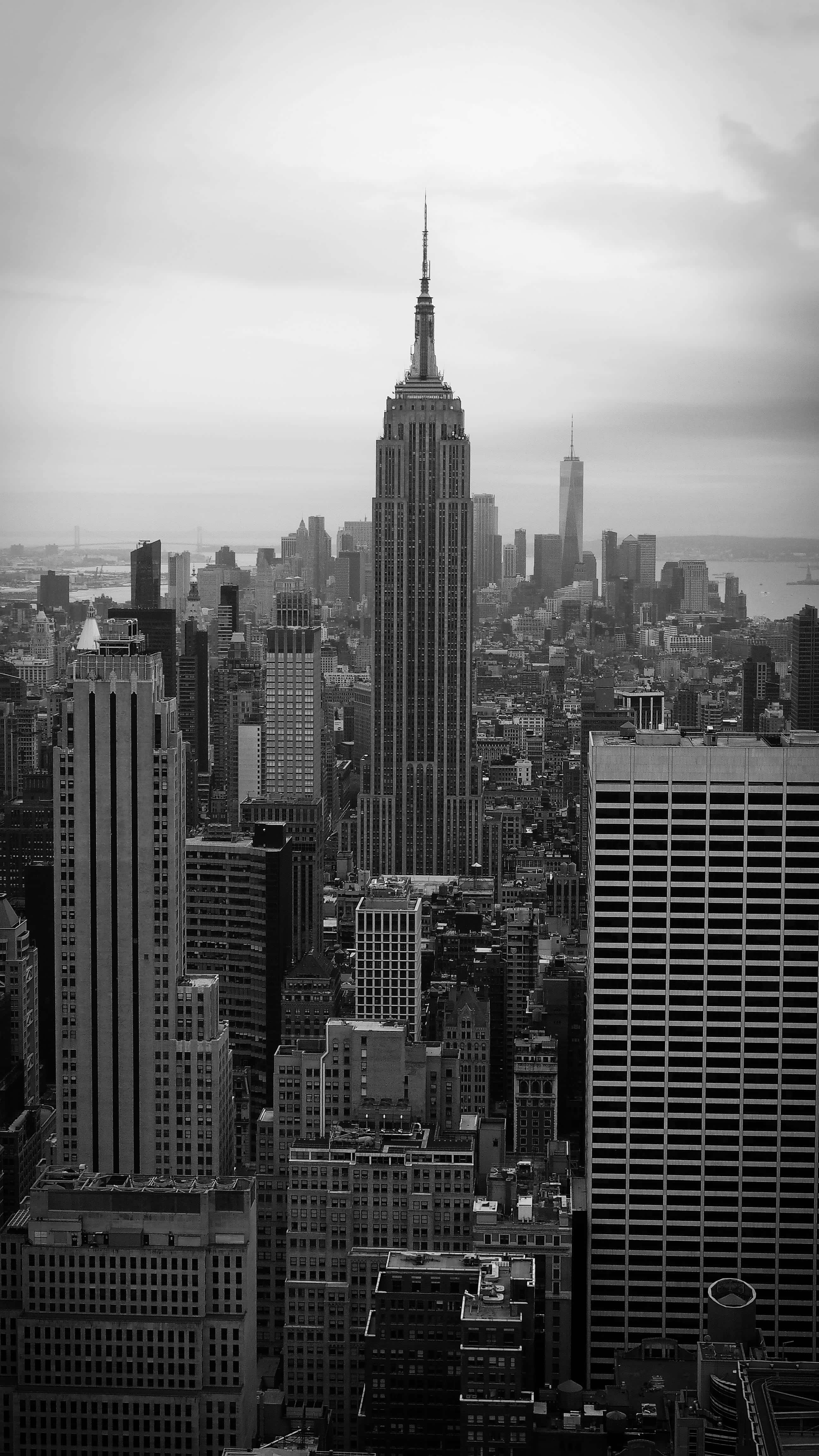 Black And White City 桌布 壁紙 — 多雲天空下，以帝國大廈為主導的紐約市天際線黑白航拍視圖。